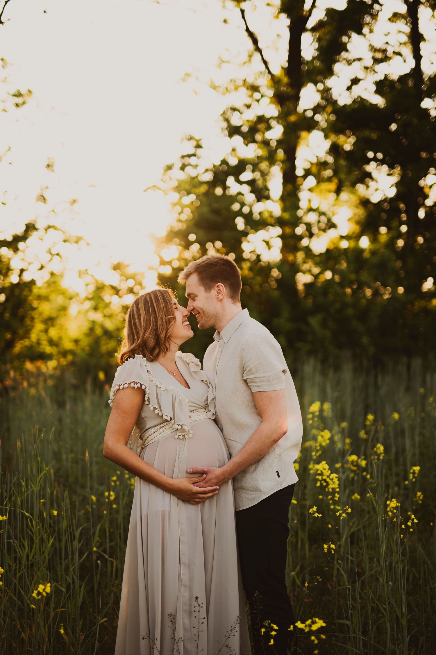 Couple embracing in golden field of flowers during sunset maternity photo session.