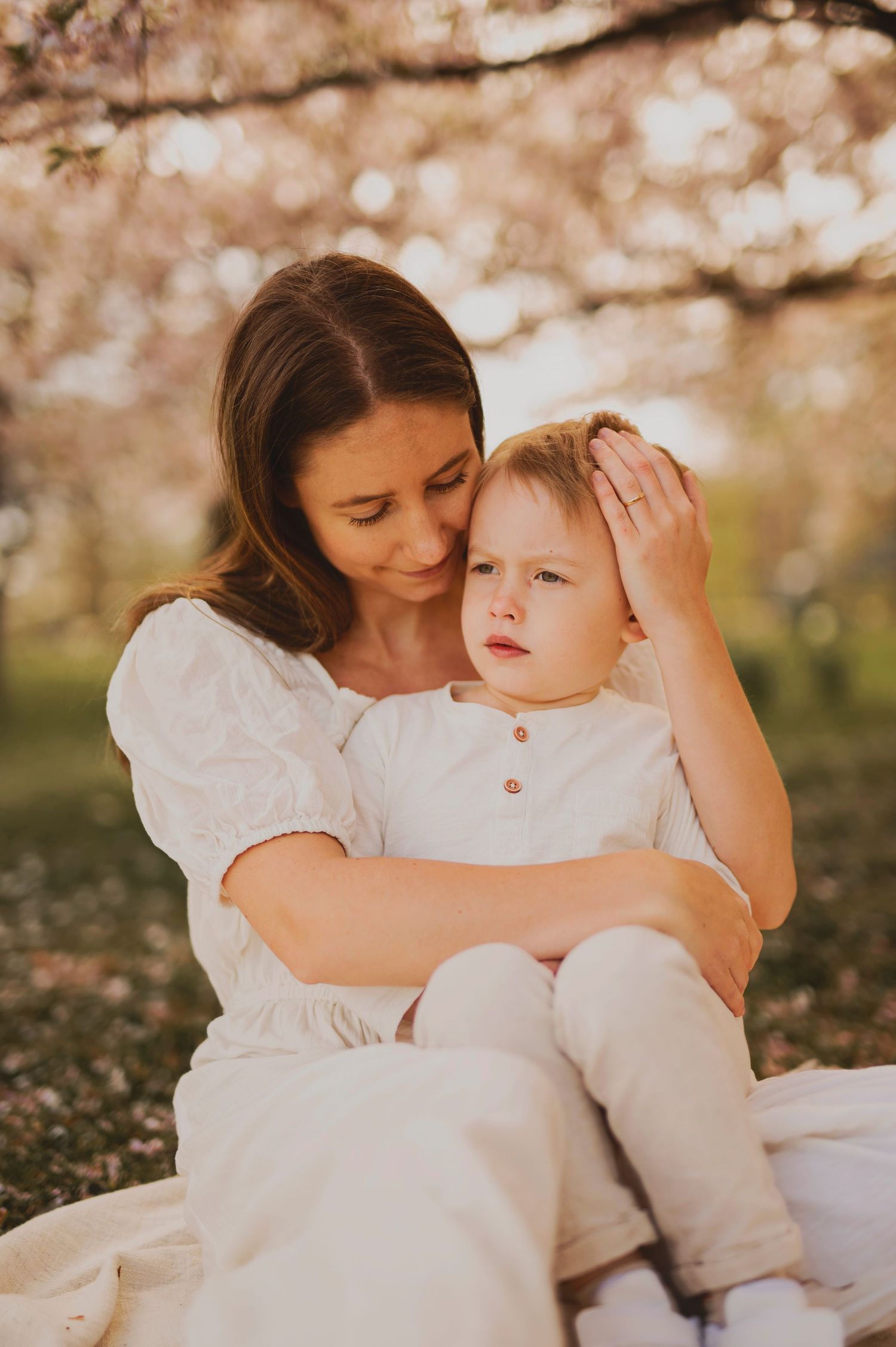 A gentle outdoor portrait with flowering trees in the background.