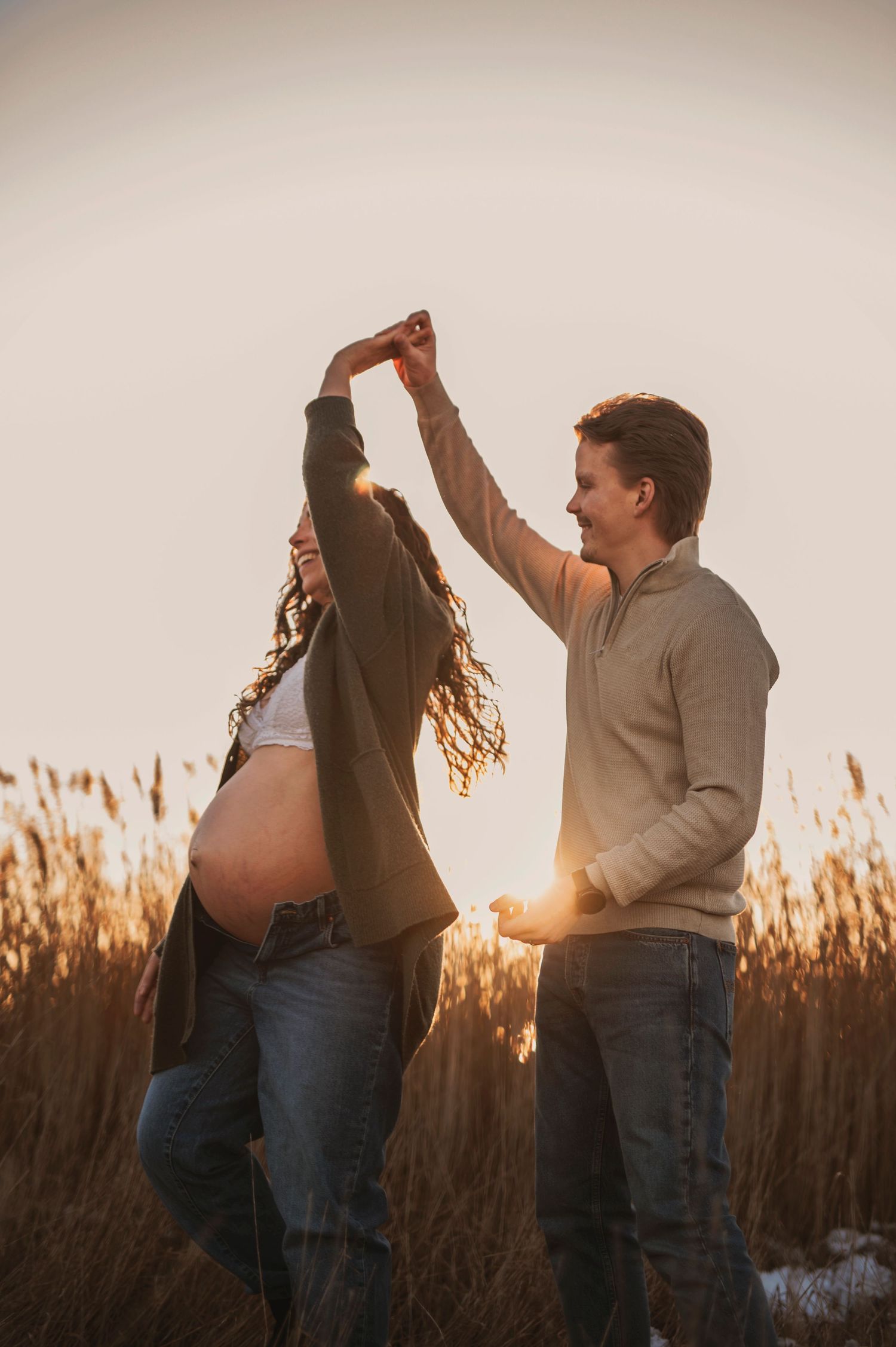 Couple dancing in golden sunlight during outdoor maternity photoshoot.