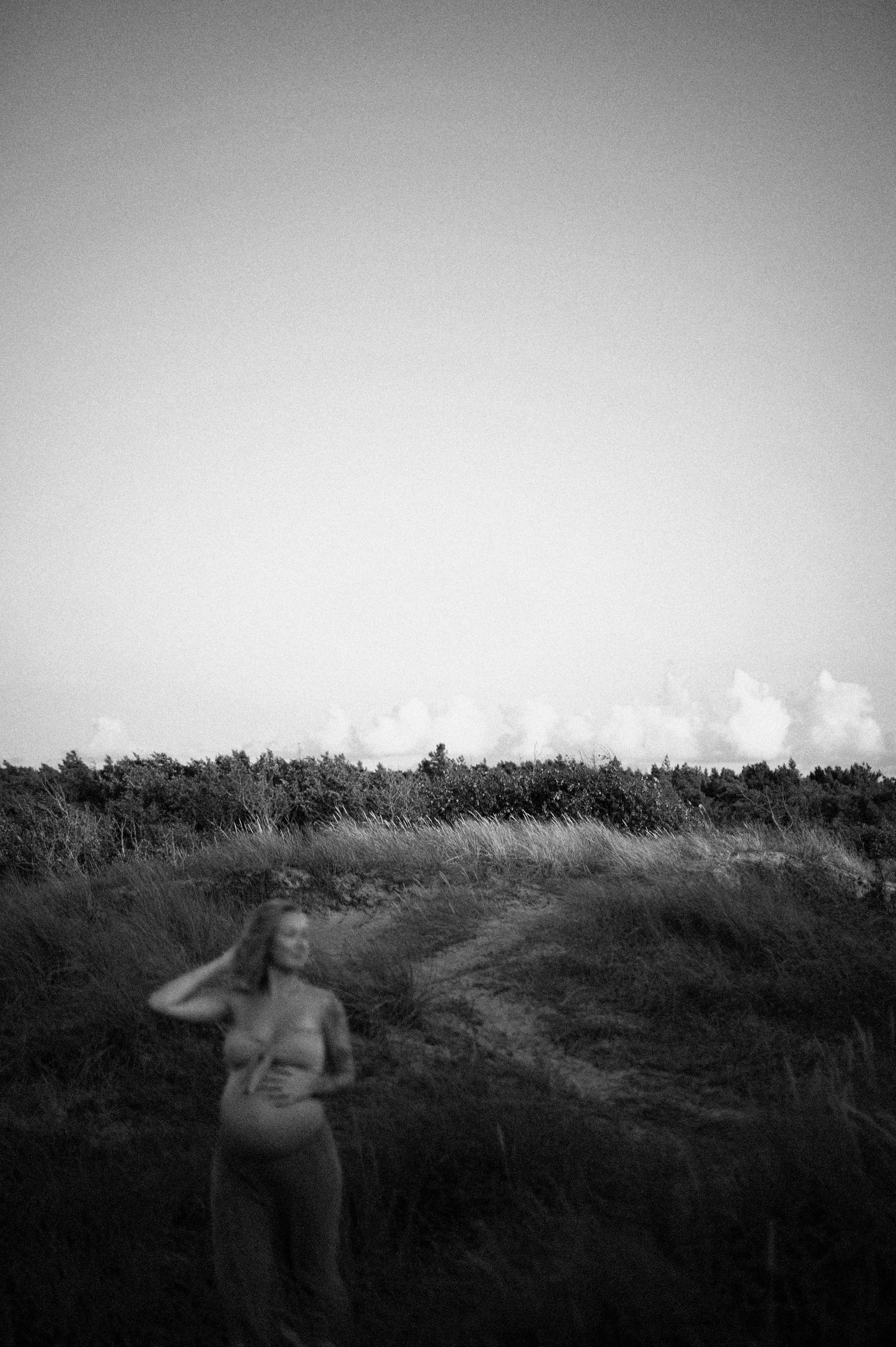A black and white artistic maternity photo silhouetted against a cloudy sky in a field.