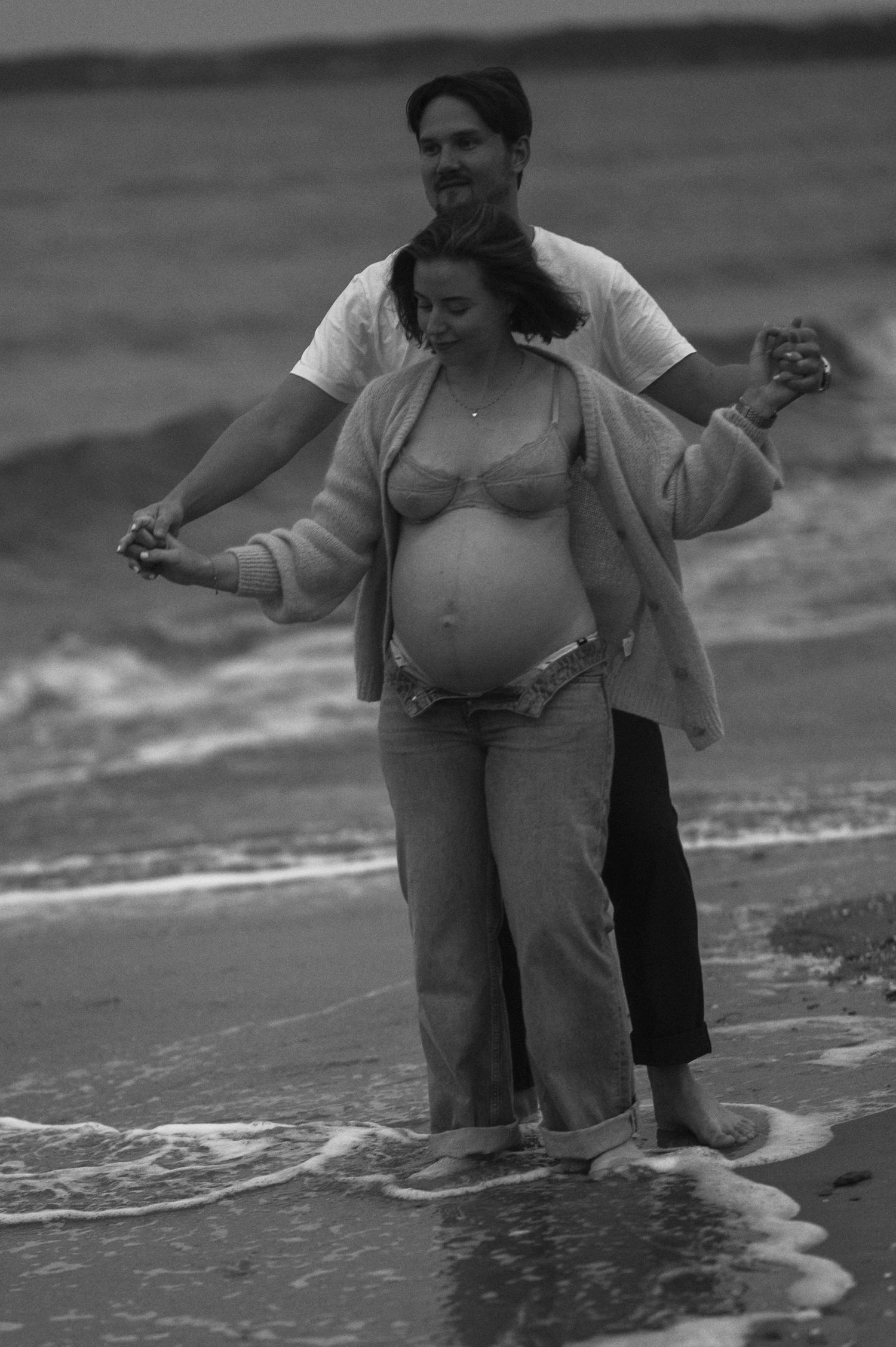 A couple stands together in the ocean waves during a beach photoshoot.
