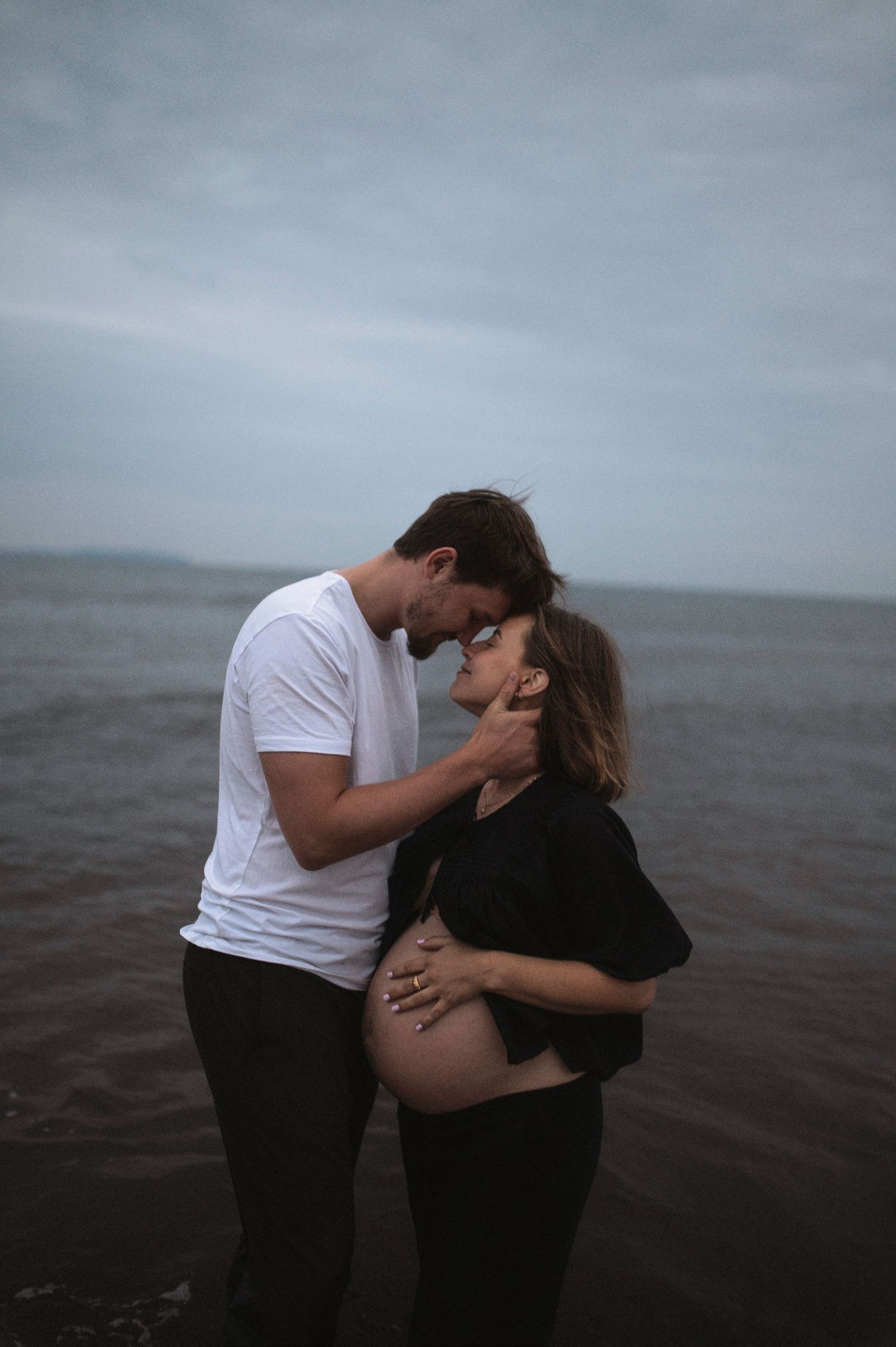Intimate moment between expectant couple standing in ocean water.