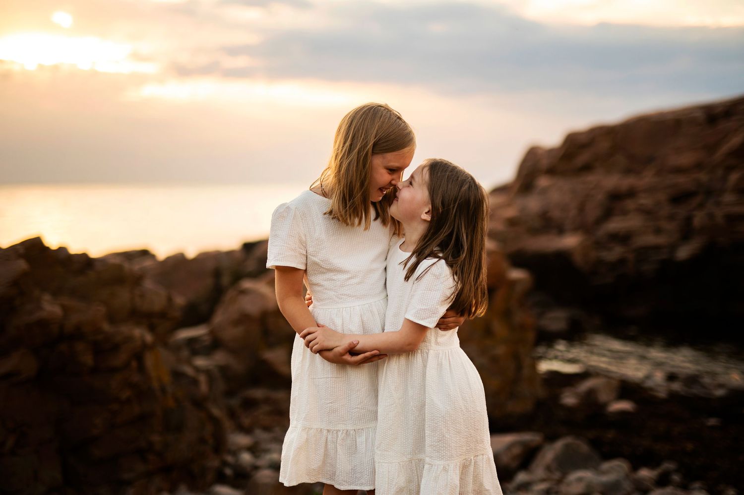 Intimate embrace during golden hour on rocky coastal landscape.