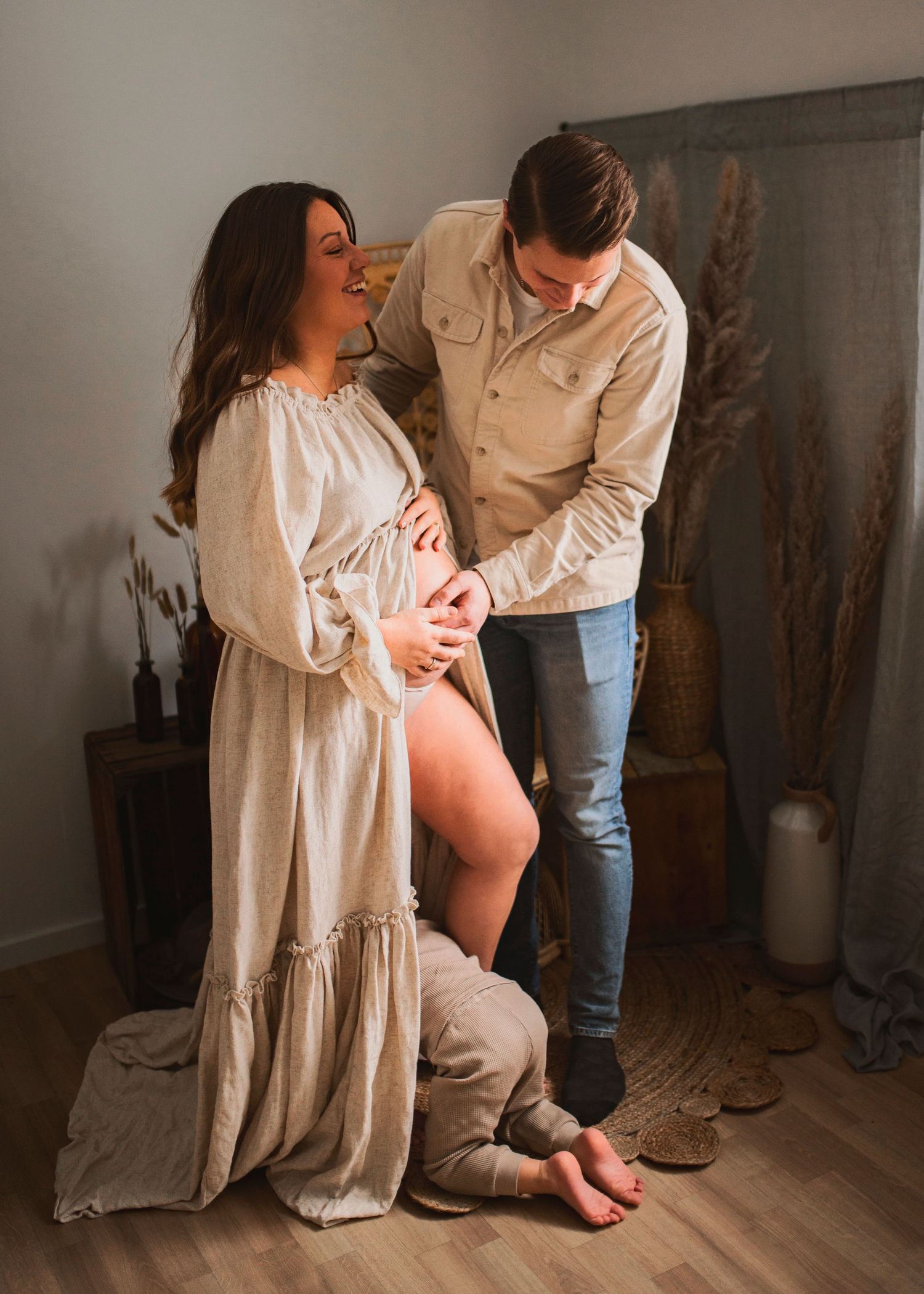 Indoor maternity portrait with couple in neutral tones sharing tender moment by dried pampas grass decor.