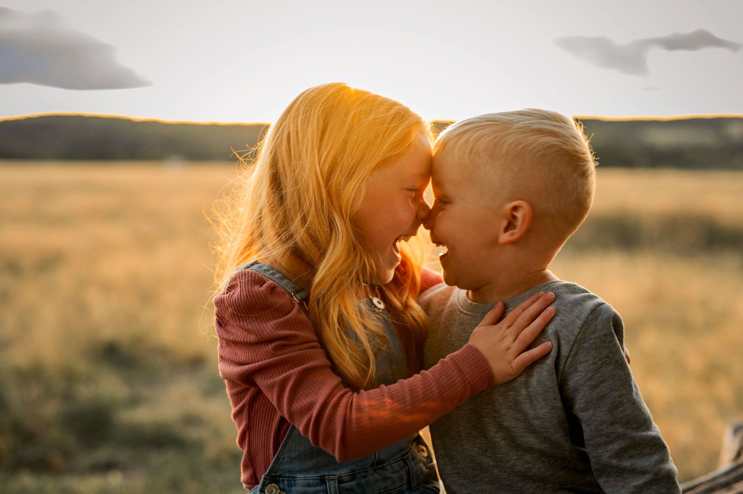 Two young children share a sweet moment in golden sunset field.