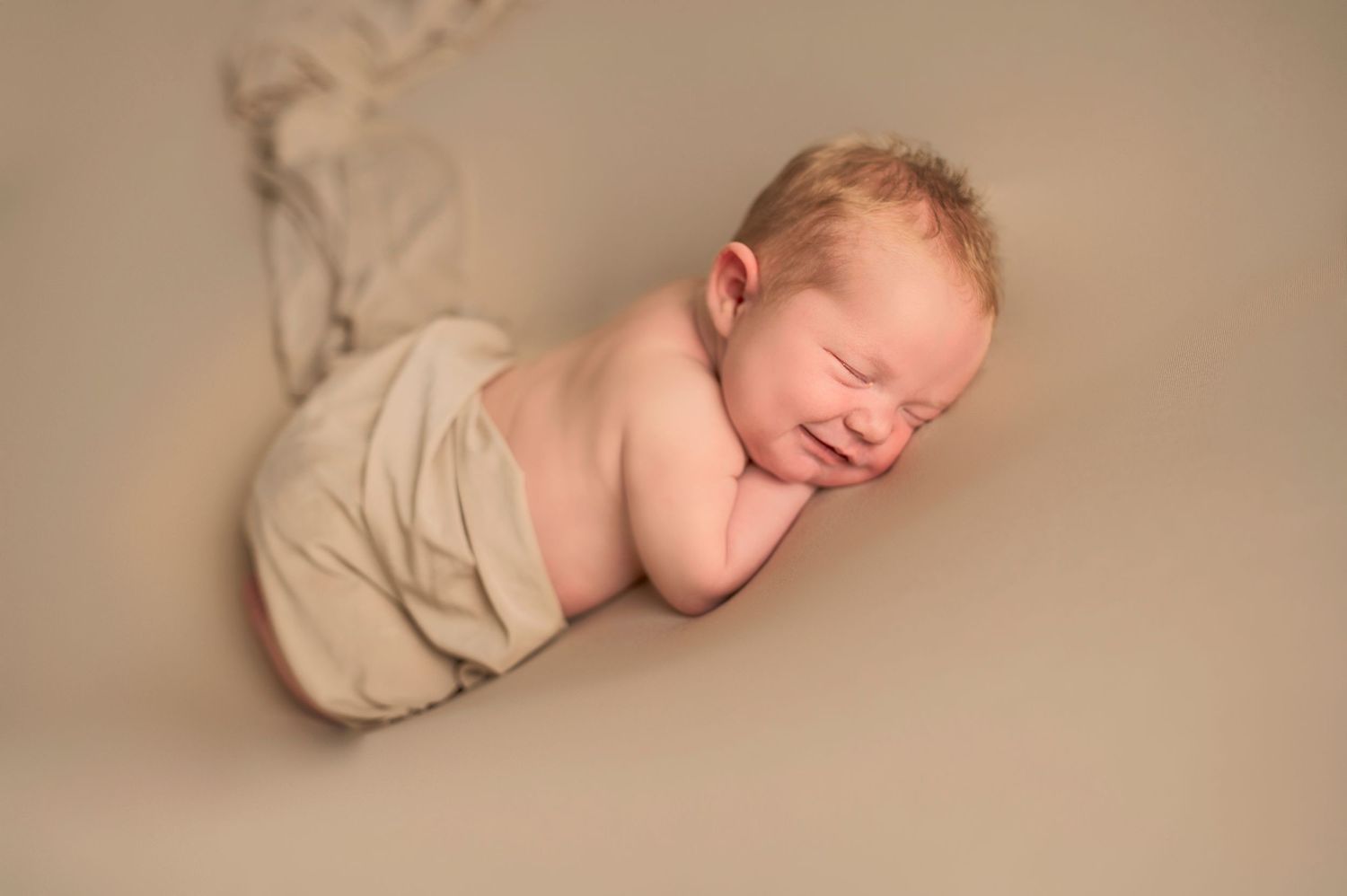 Sleeping newborn wrapped in light fabric rests against neutral background in studio setting.