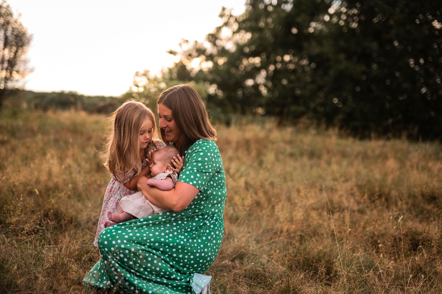 Two people sharing an intimate embrace in a sun-drenched field while wearing a green polka dot dress.
