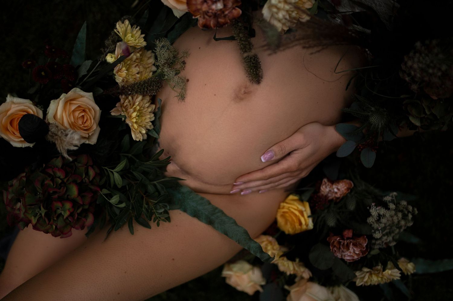 Artistic pregnancy photo surrounded by yellow and pink flowers.