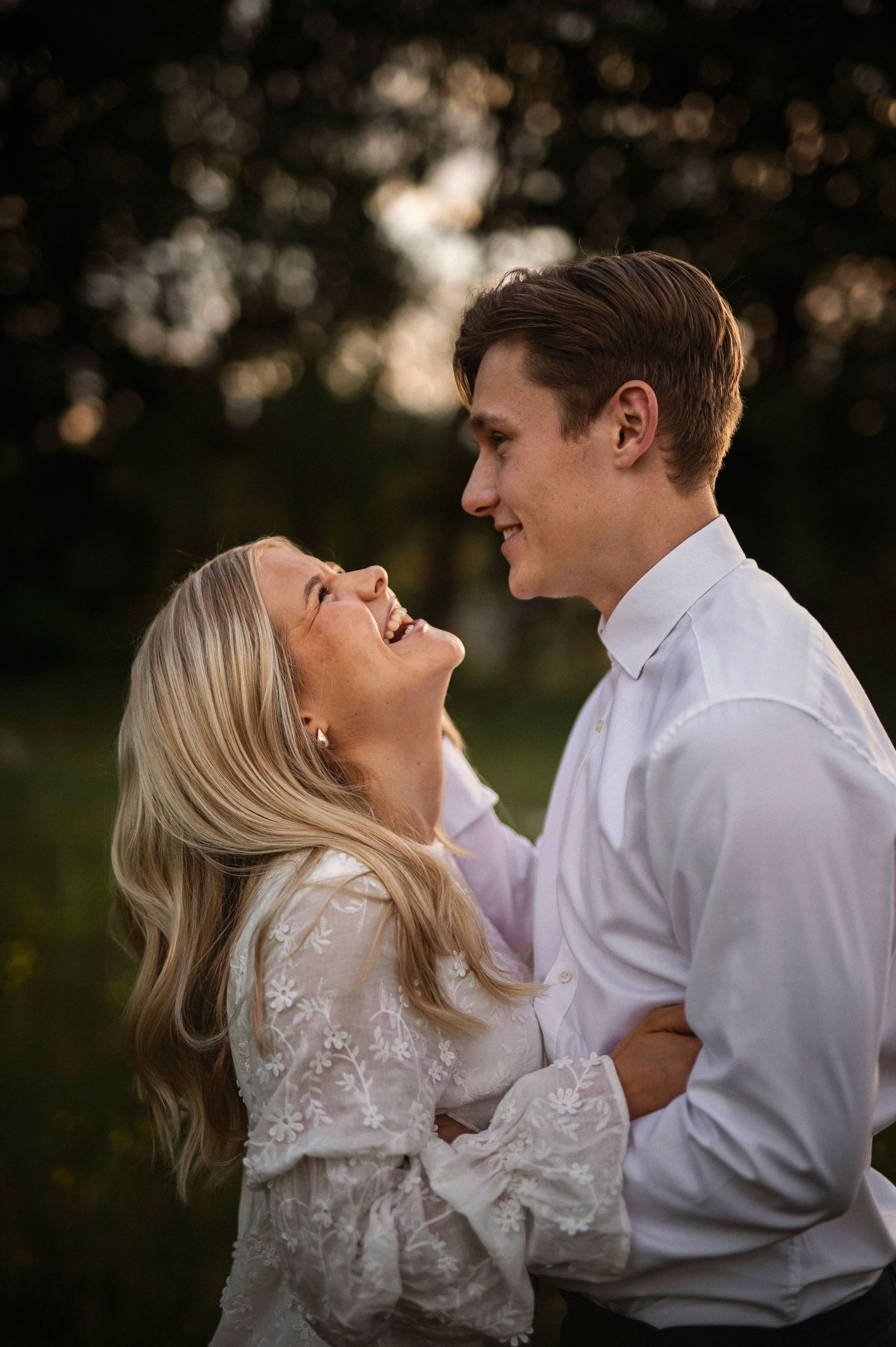 A joyful couple laughs together outdoors in warm golden sunset light.