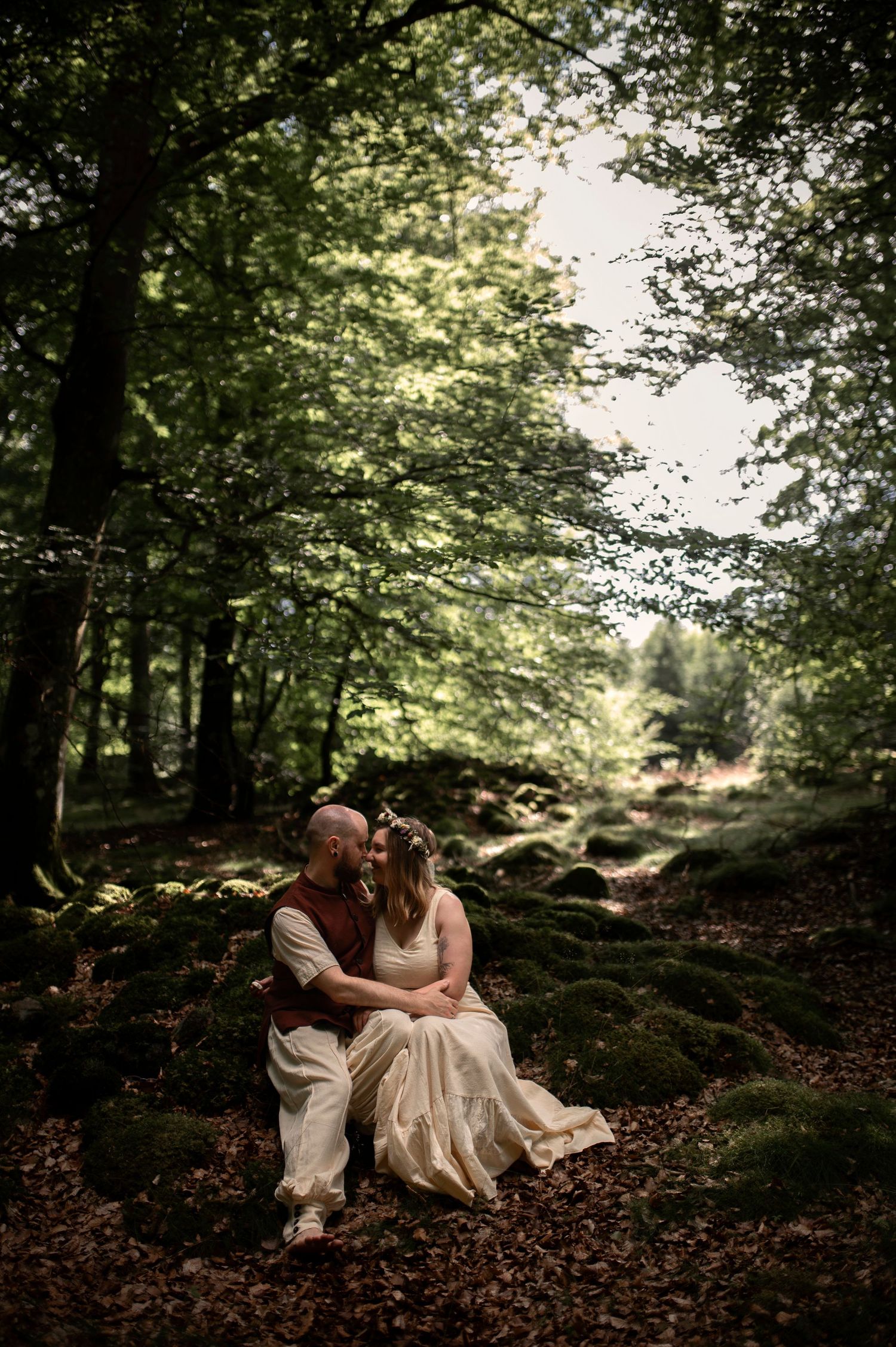 Newlywed couple sitting on mossy rocks in a lush green forest during their wedding day.