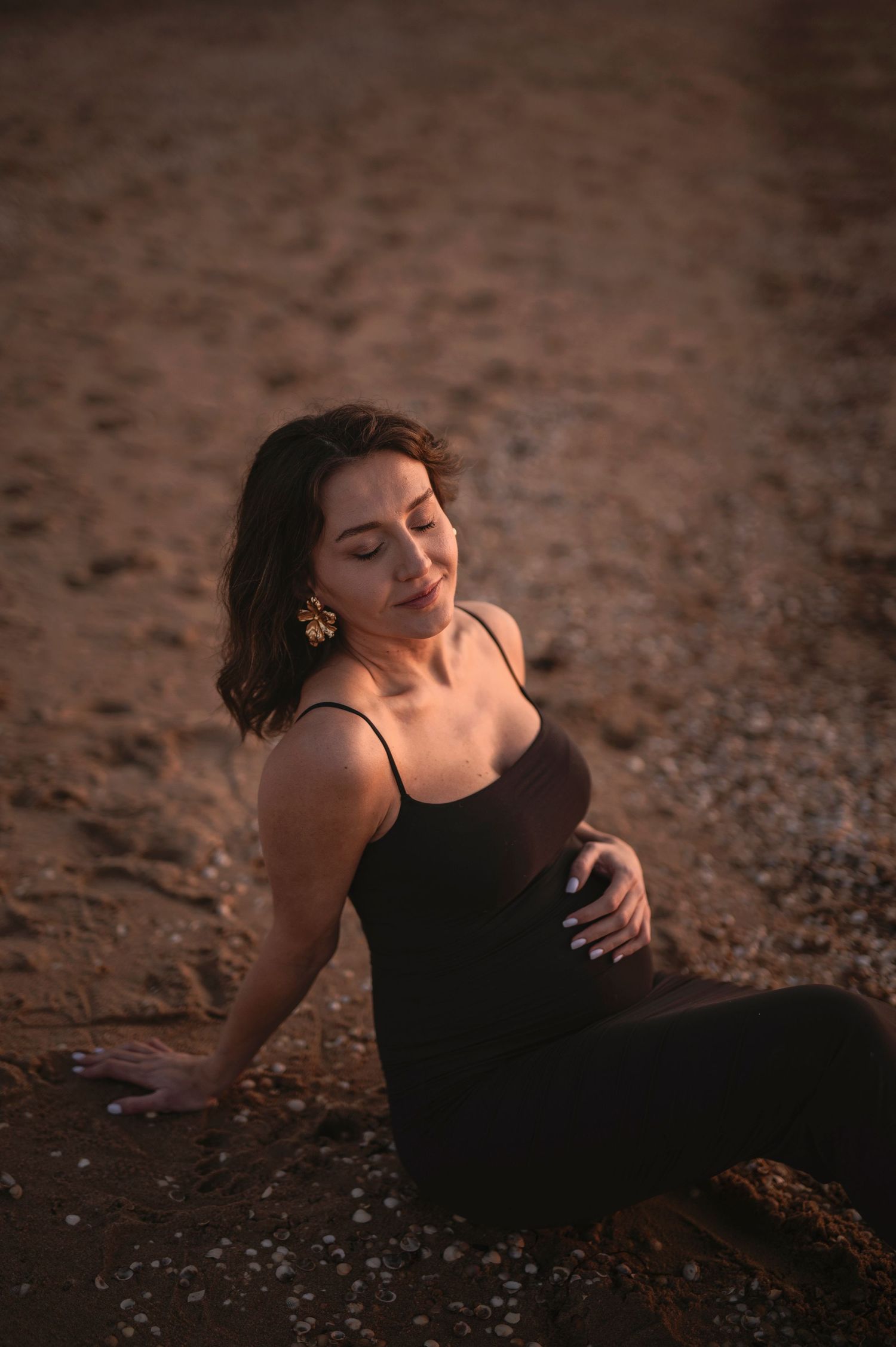 Maternity portrait on sandy beach at dusk showing expecting mother in black dress.
