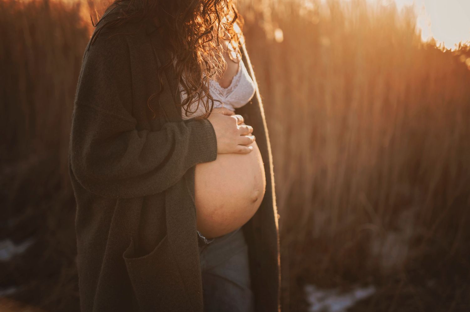 Side view of pregnant belly at sunset with tall grass in background.