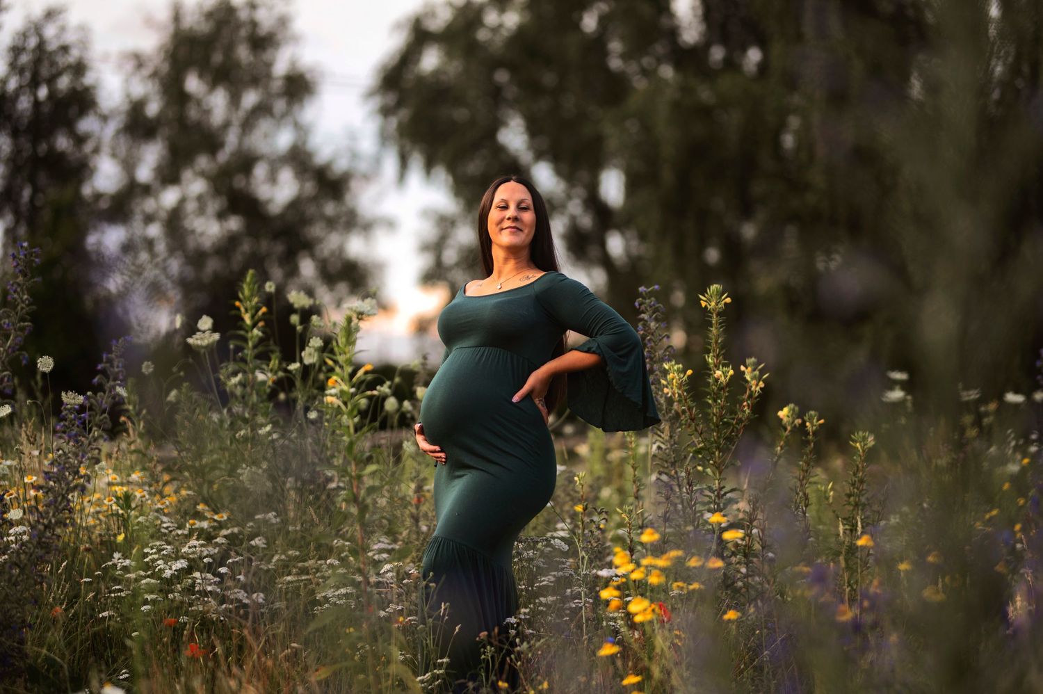 Expecting mother in blue dress poses among wildflowers during golden hour.