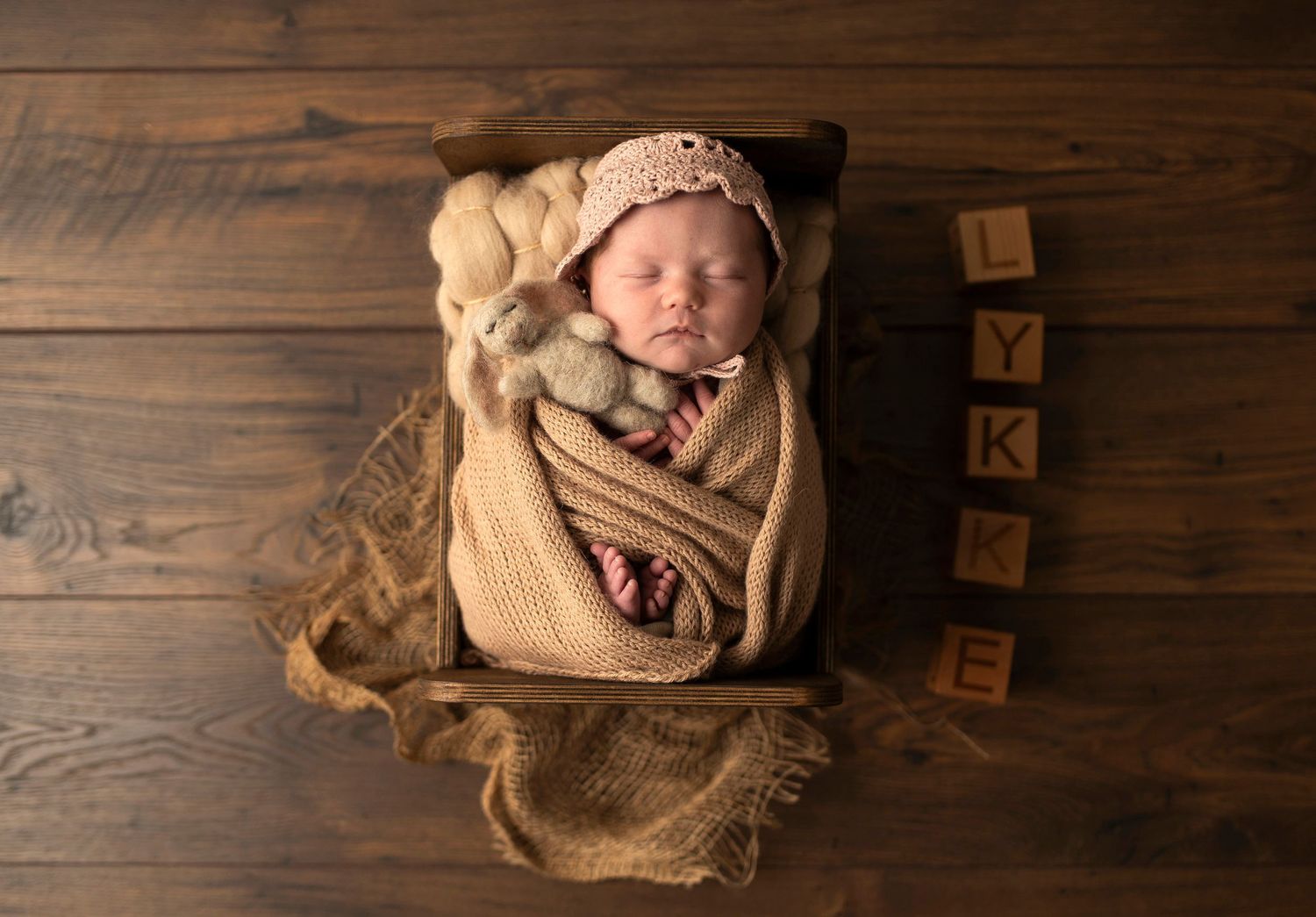 Sleeping newborn wrapped in beige blanket with wooden letter blocks as decoration.