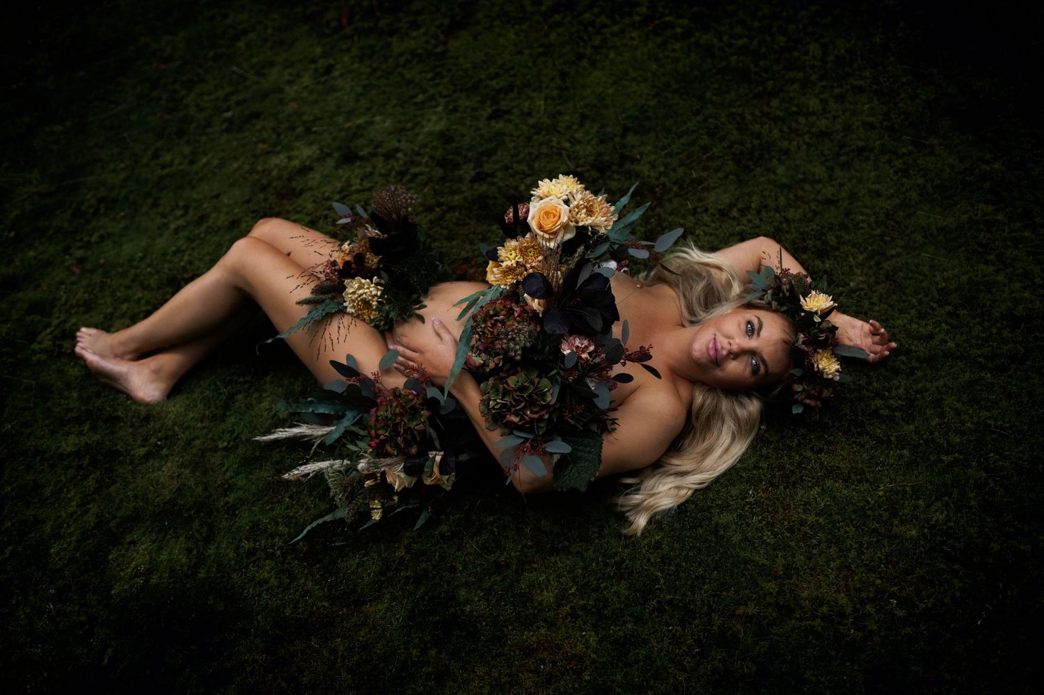 Dramatic maternity photography with yellow roses and dark foliage.