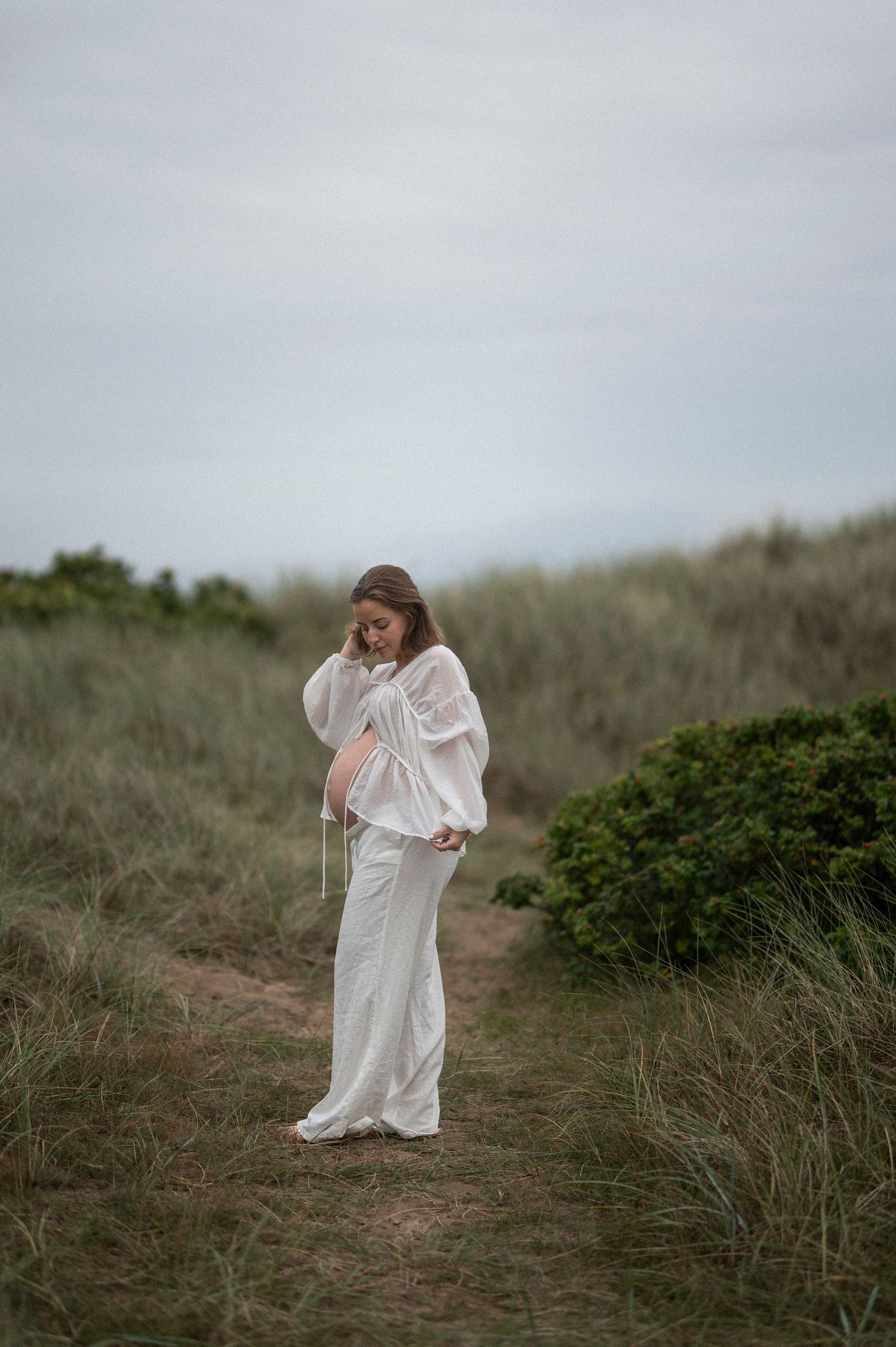 A serene maternity portrait taken on a coastal hill with muted natural tones.