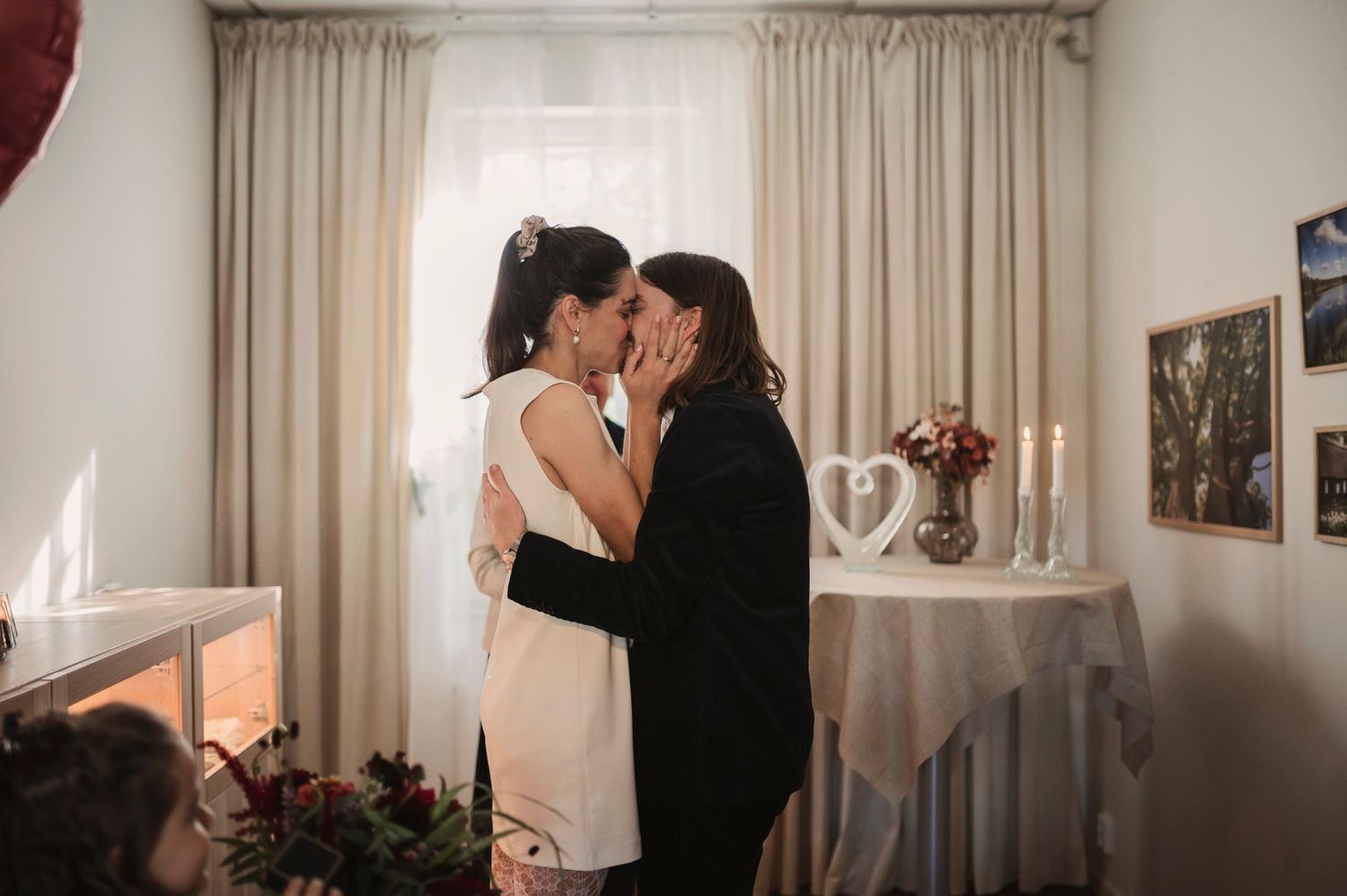 Indoor wedding portrait of couple sharing intimate moment near curtained window.