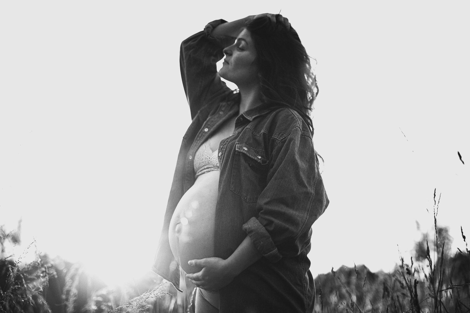 A high contrast black and white photo shows an expectant mother in a natural setting.