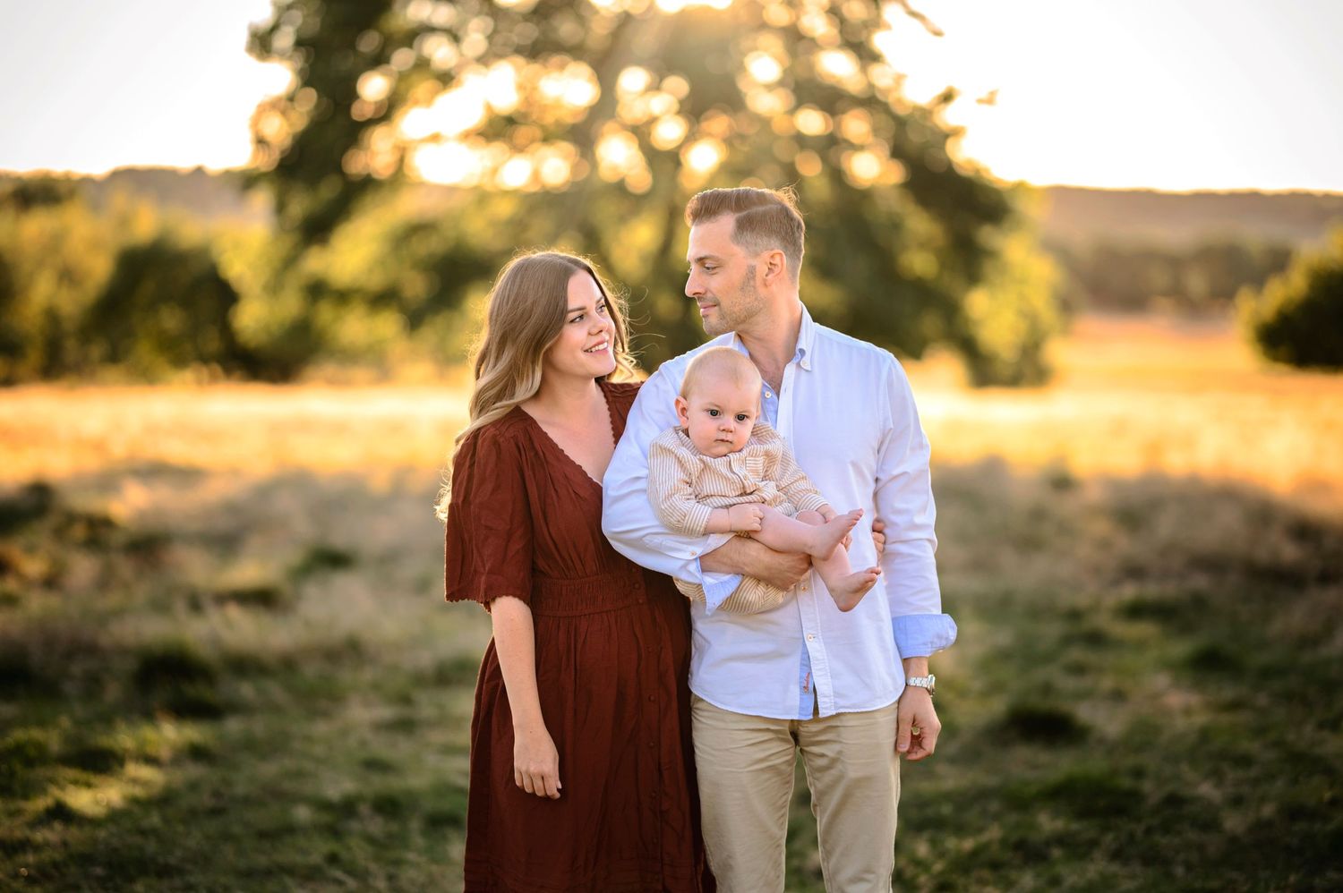 Family portrait in outdoor field with sunset lighting and coordinated outfits.