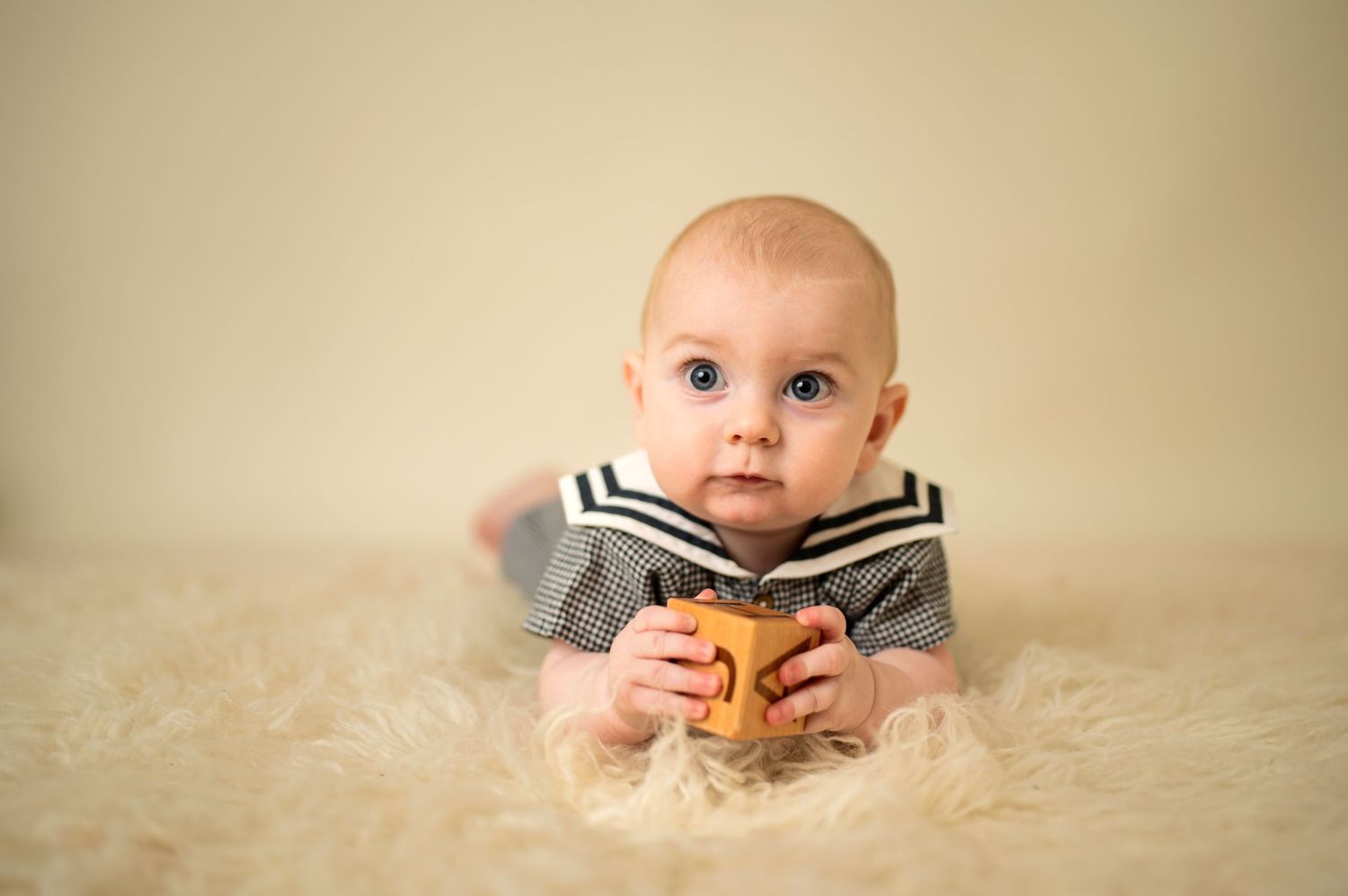 Baby in striped outfit lying on fluffy white rug.