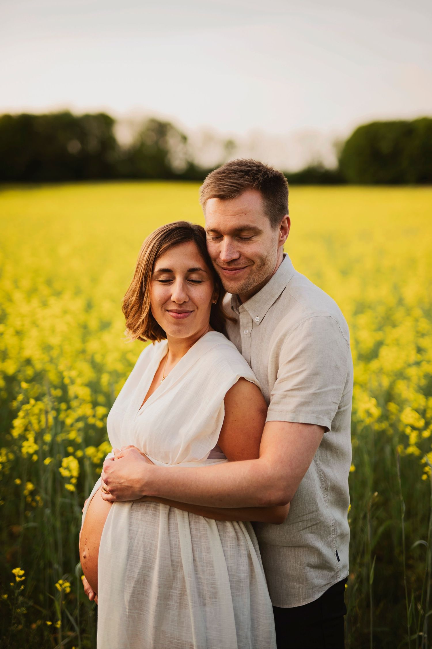 Maternity portrait of couple embracing in yellow flower field during sunset.