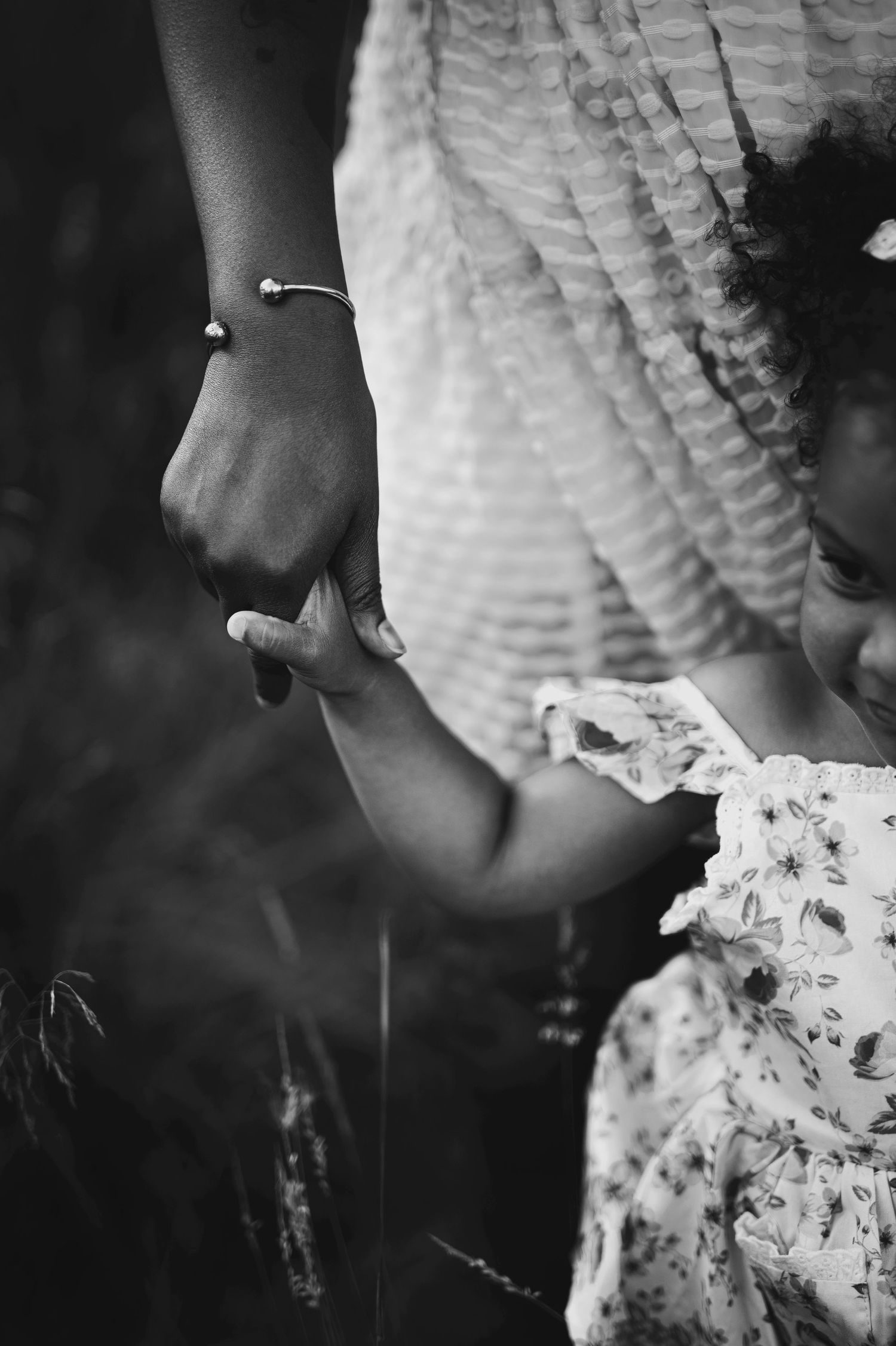 A black and white close-up of hands holding each other, with one wearing a delicate bracelet.