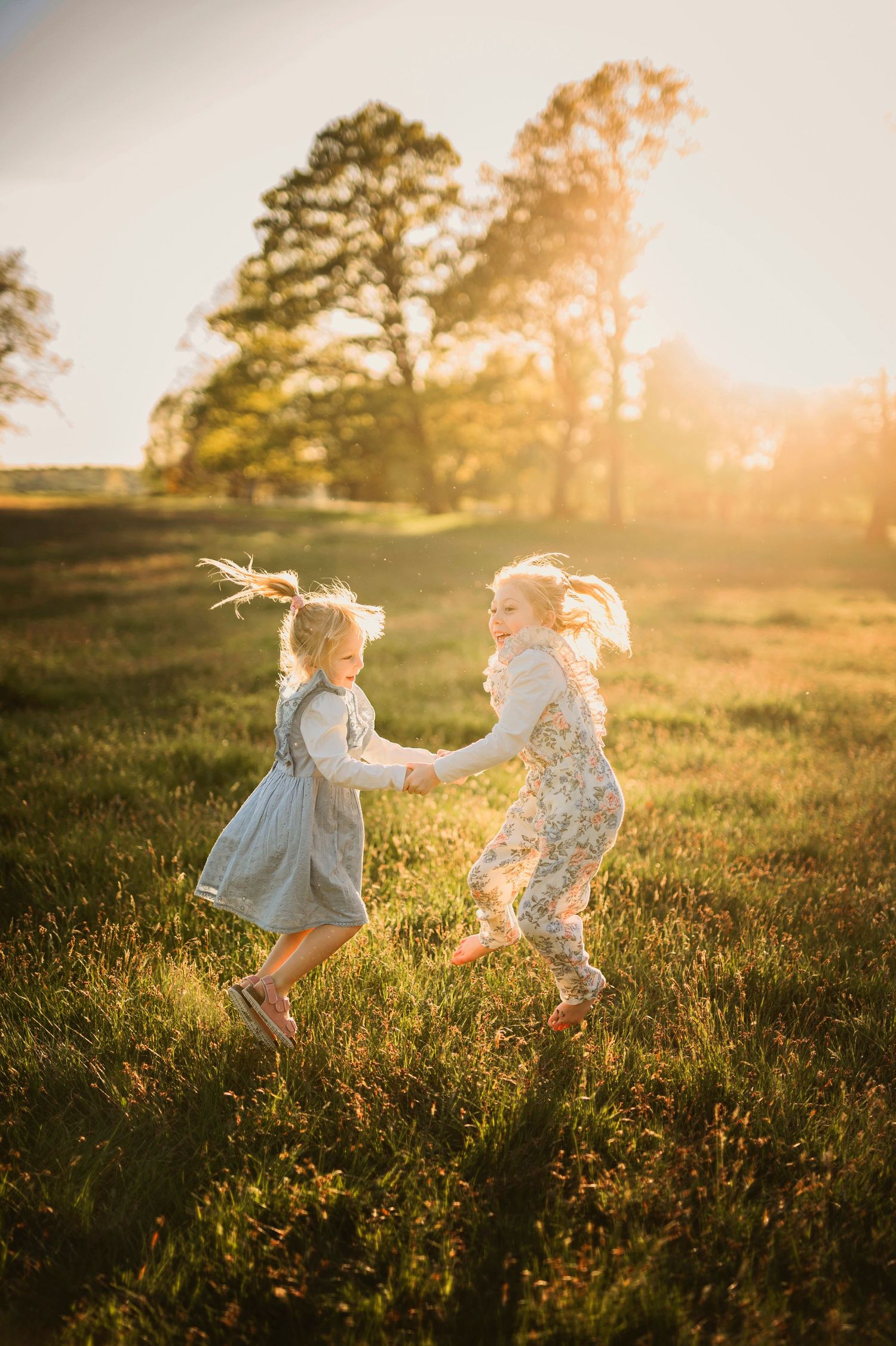 Two children dancing and playing together in a sunlit meadow with trees in background.