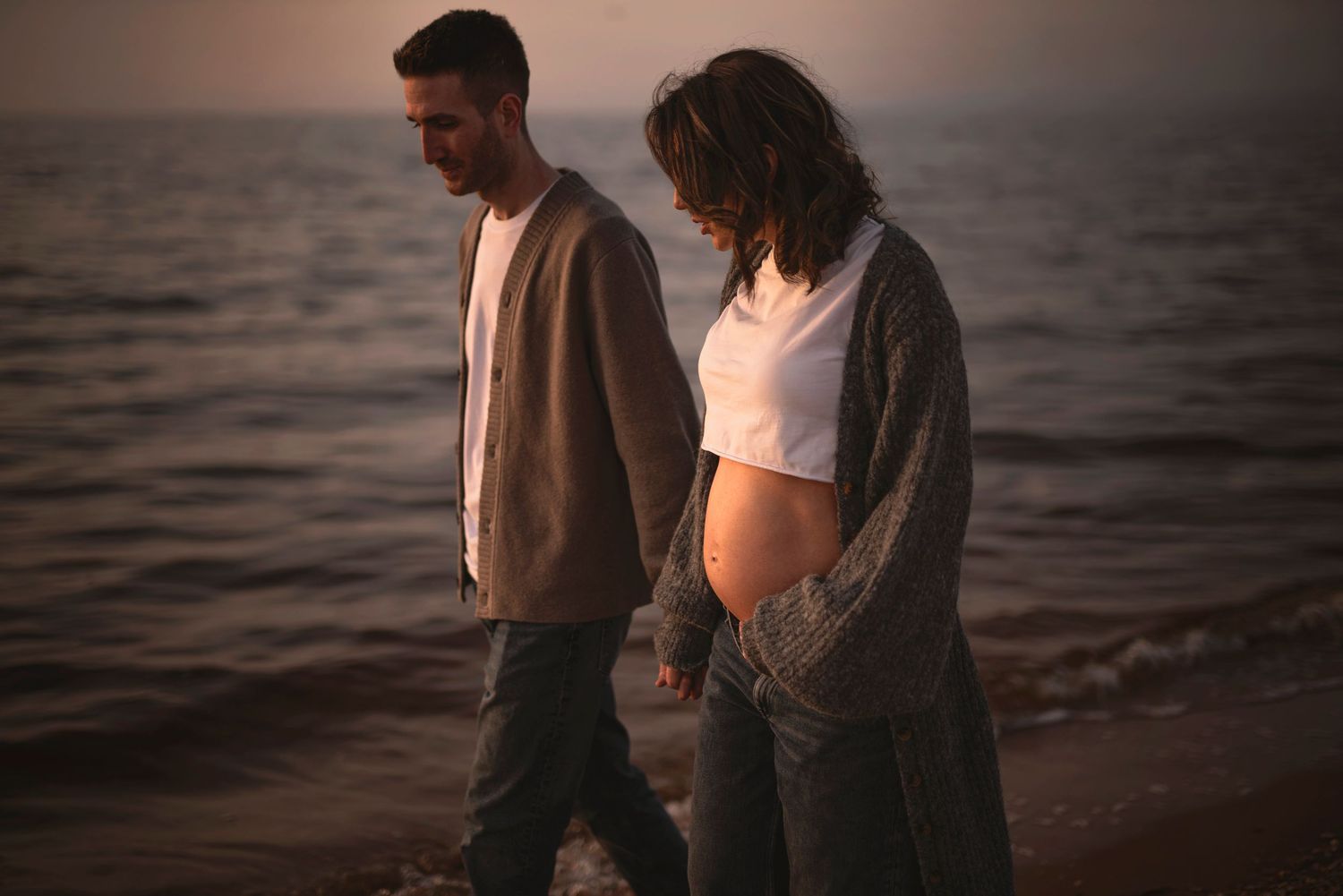 A couple walks along a misty beach at sunset wearing casual sweaters and enjoying the serene oceanfront atmosphere.