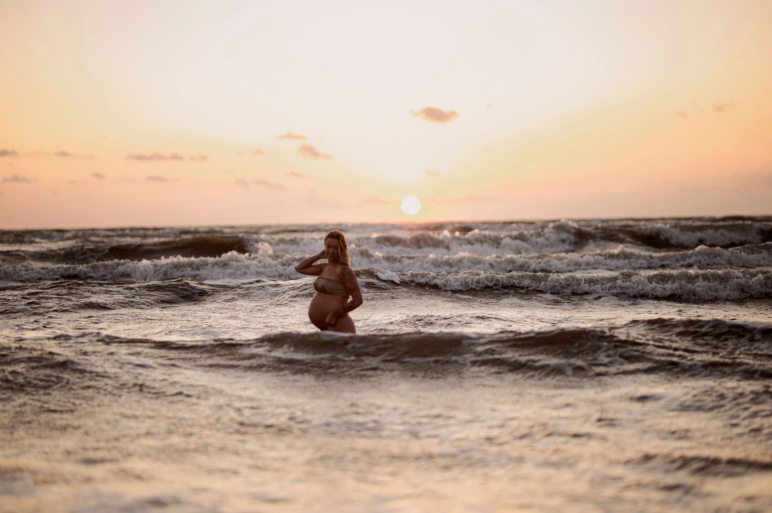 A silhouette stands in shallow ocean waves during a vibrant beach sunset.