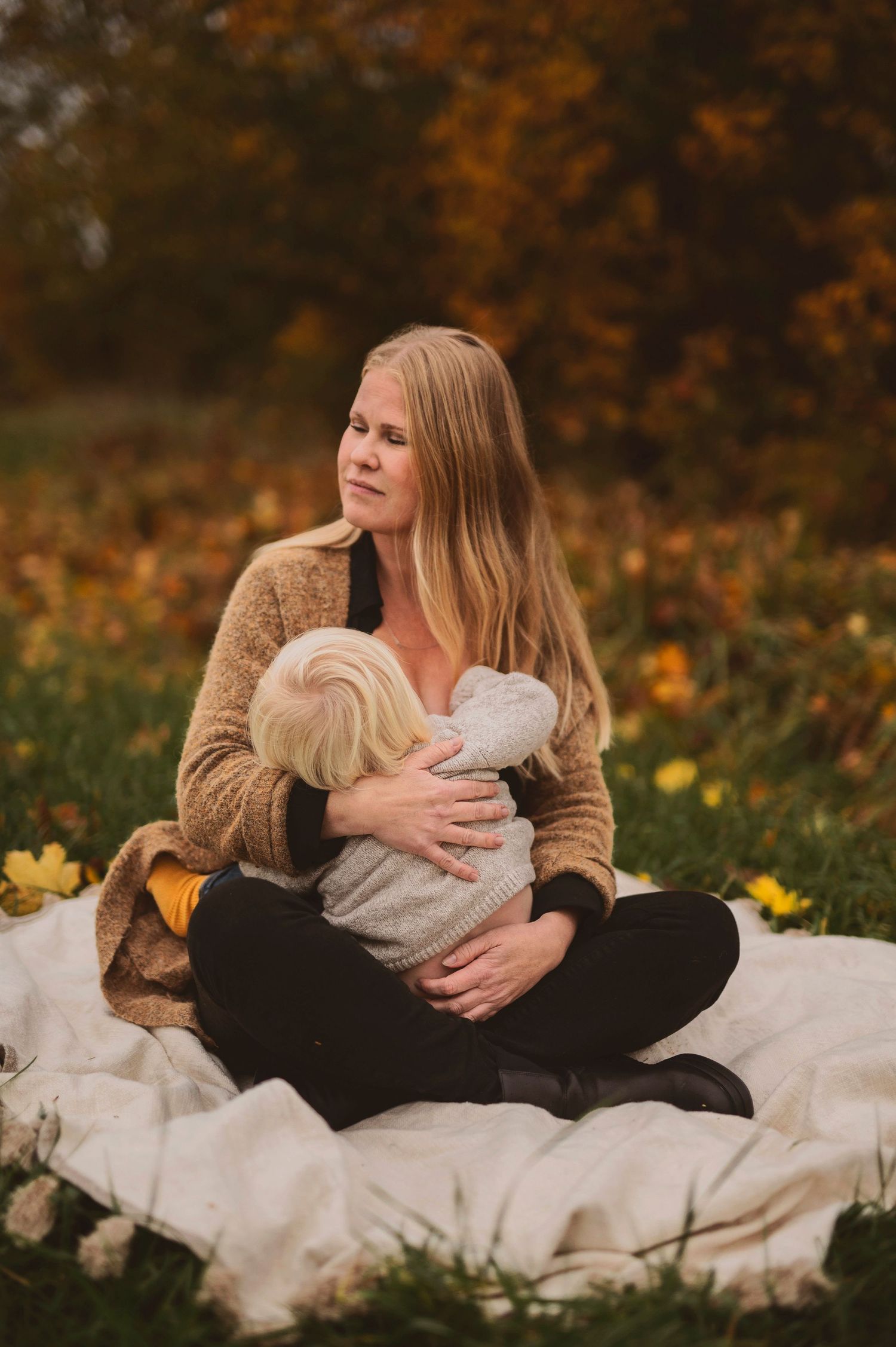 Natural breastfeeding portrait on white blanket with autumn scenery behind.