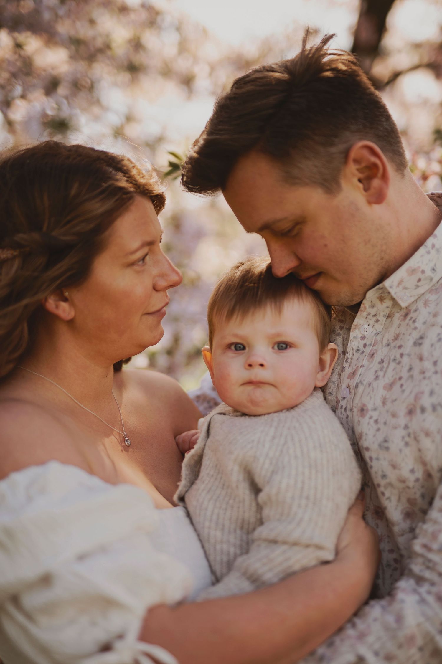 A tender family portrait captured under flowering spring trees in warm golden light.