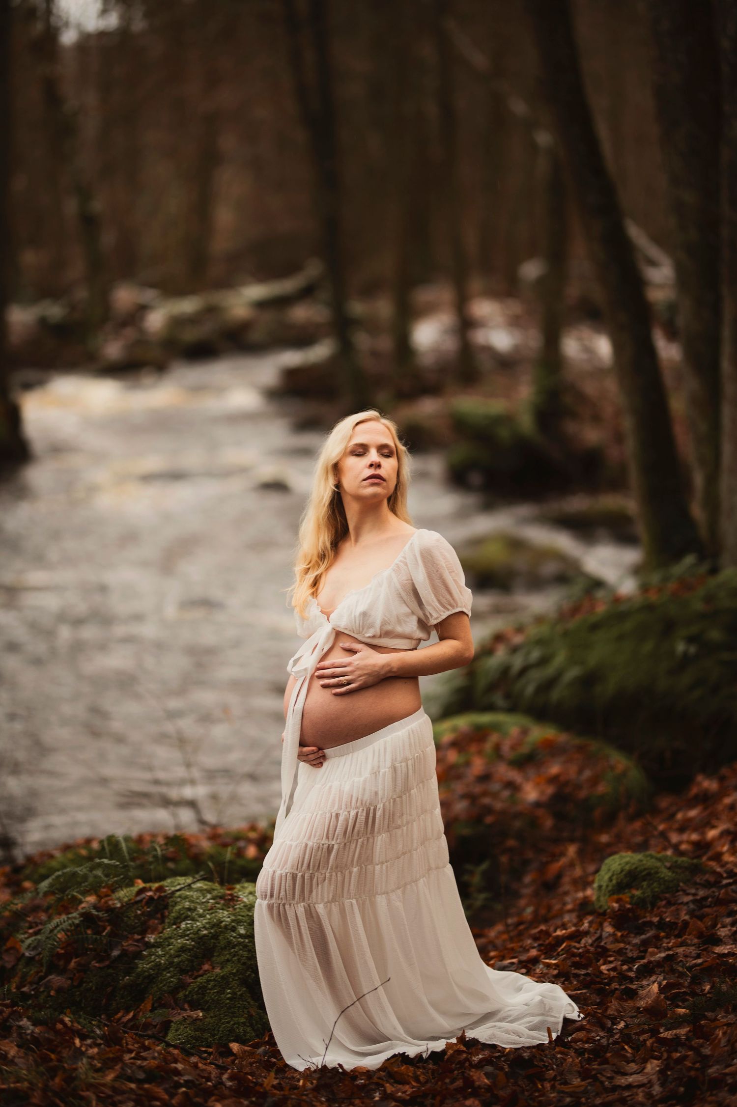 Vacker gravid kvinna på fotografering vid en bäck. Fotograf är Lovestories By Sara.