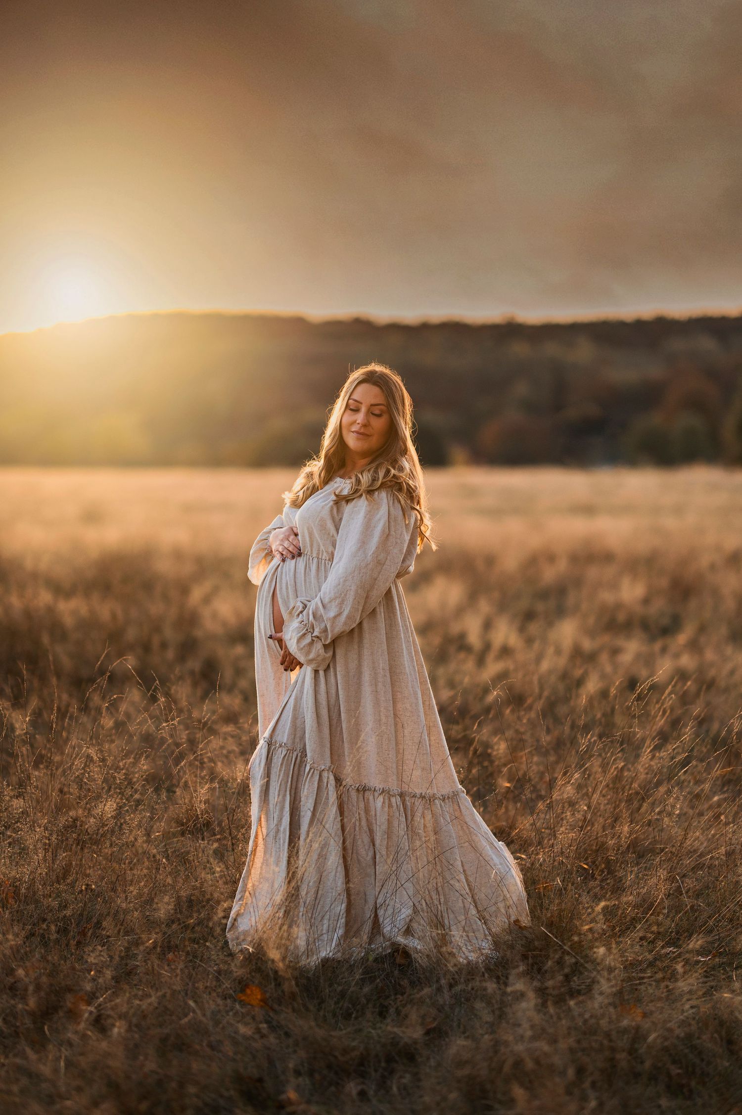 Person in flowing white dress poses in golden field at sunset.