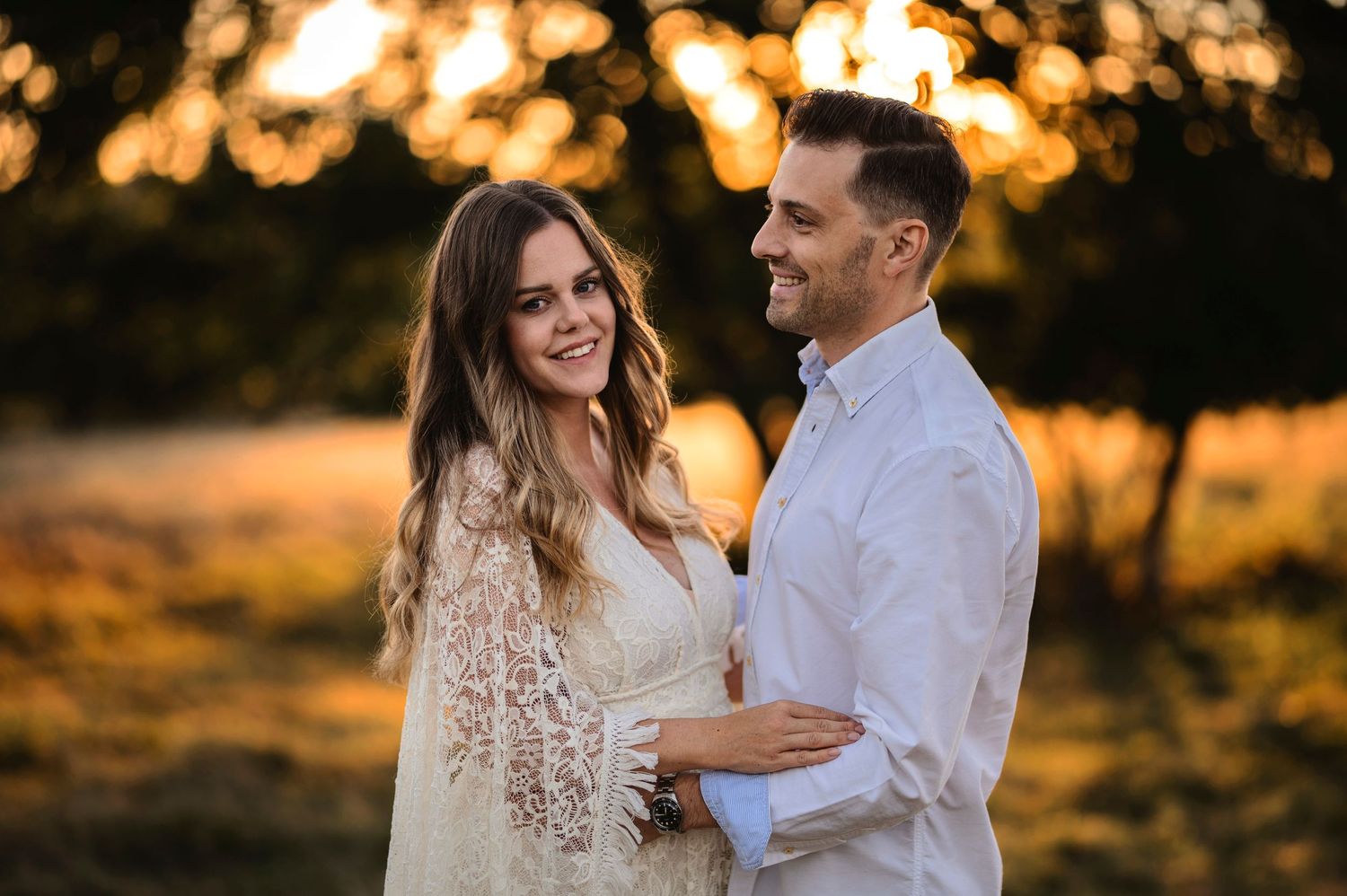 A couple in white clothing shares a loving embrace during sunset.