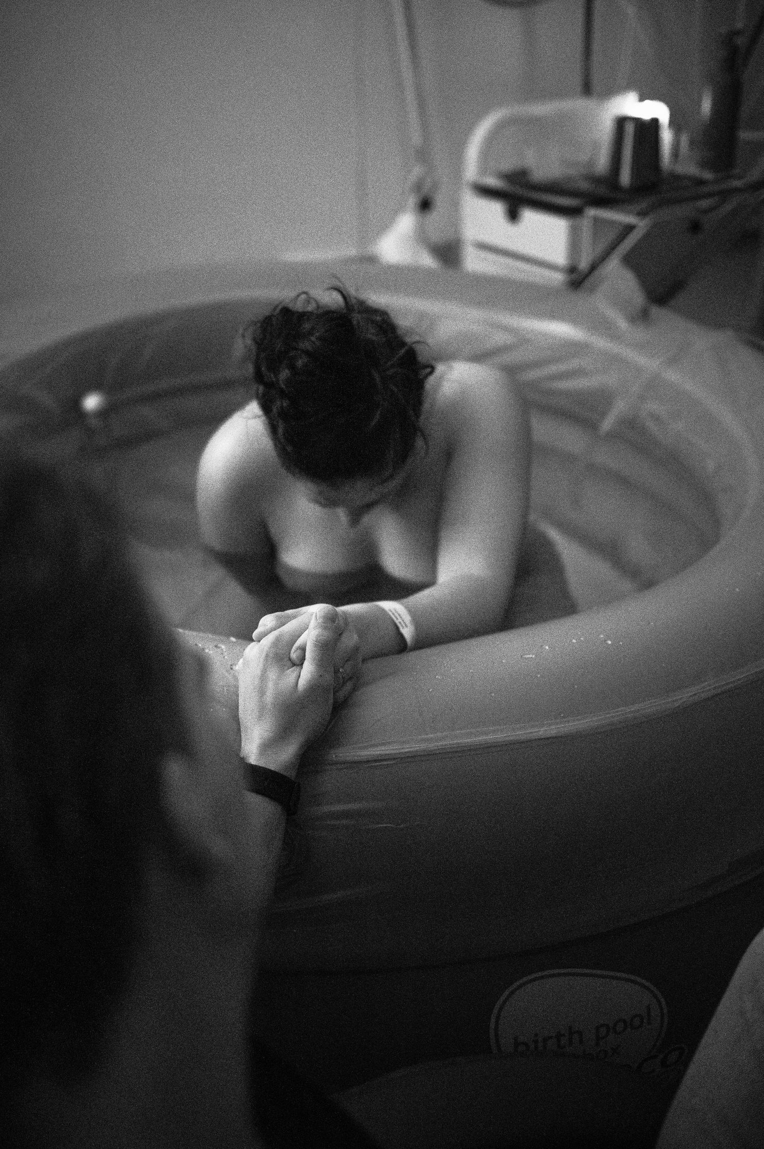 A woman laboring in a birth pool during water birth, holding hands with a support person beside her.
