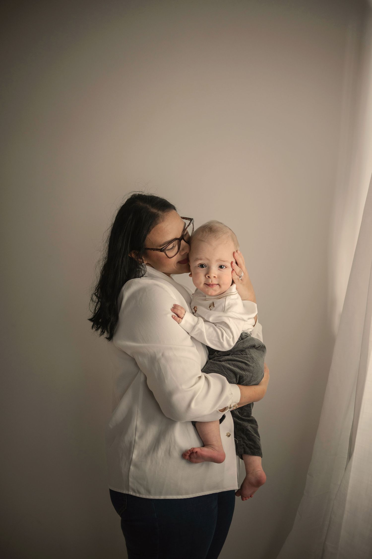 A tender moment captured against a dark background shows a parent in white embracing a young baby.