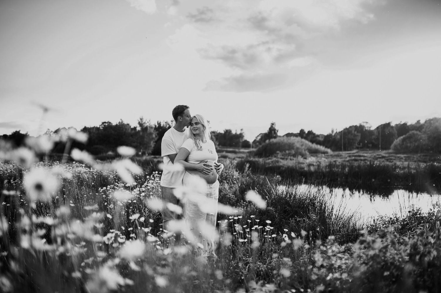 Black and white panoramic shot of a daisy field maternity session near water.