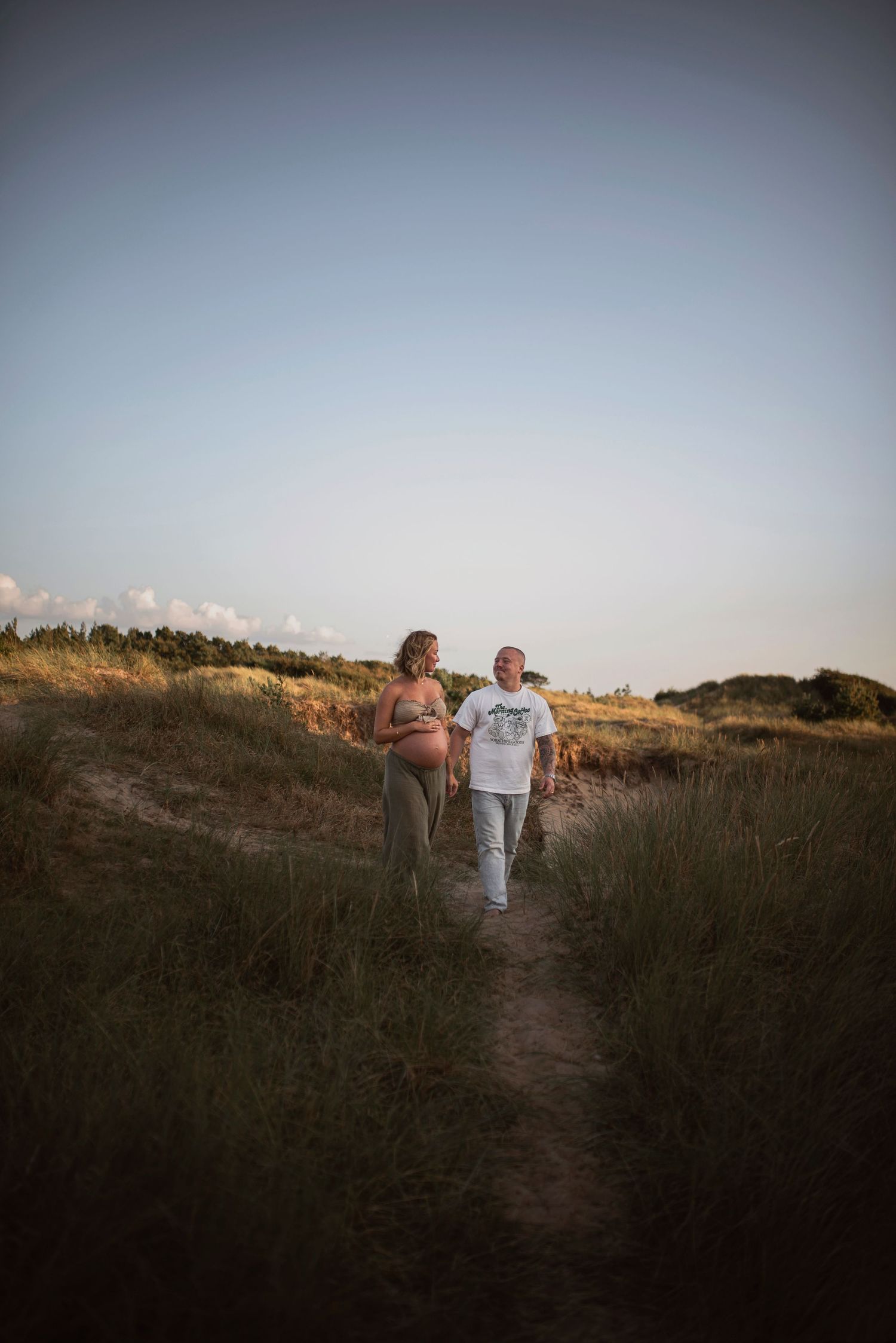 A couple walks together along a scenic coastal path during golden hour.