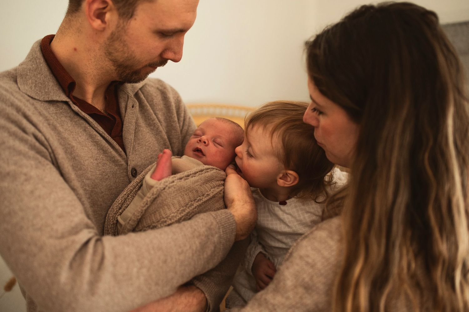 Family sits together on couch sharing tender moment with new baby.