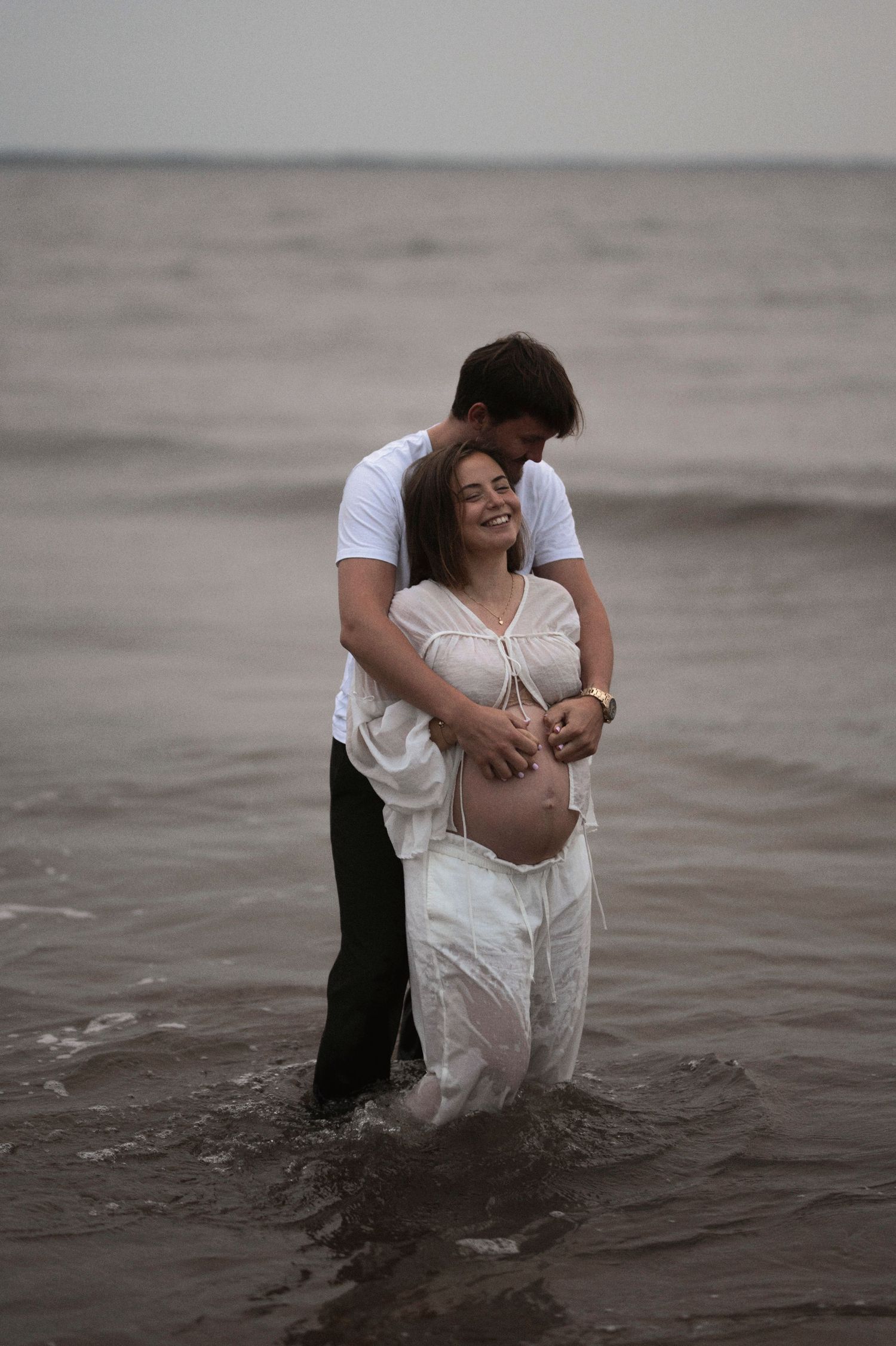 Intimate moment captured of a couple standing in shallow ocean waters during a maternity shoot.