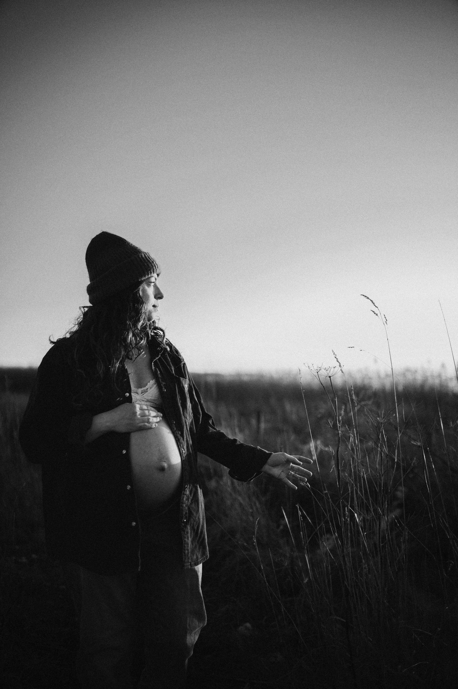 Winter maternity portrait in black and white with subject touching tall grass.