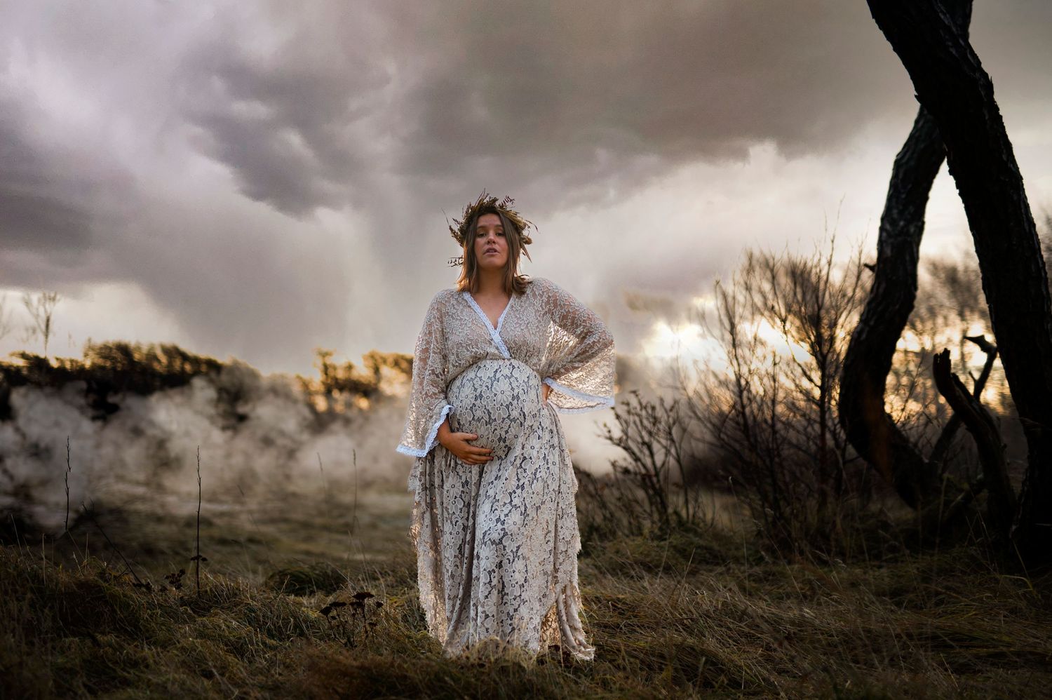 Dramatic maternity portrait with stormy skies and misty atmosphere in natural landscape setting.