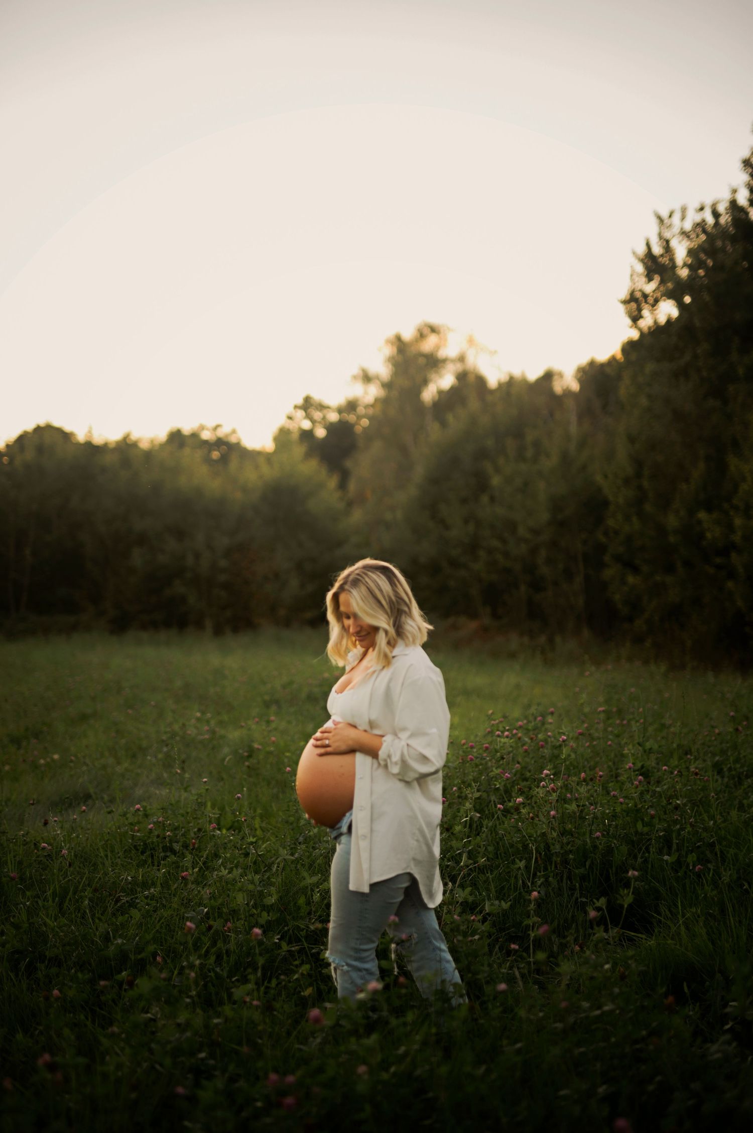 Maternity photoshoot in a golden field at sunset showing an expecting mother holding her belly.