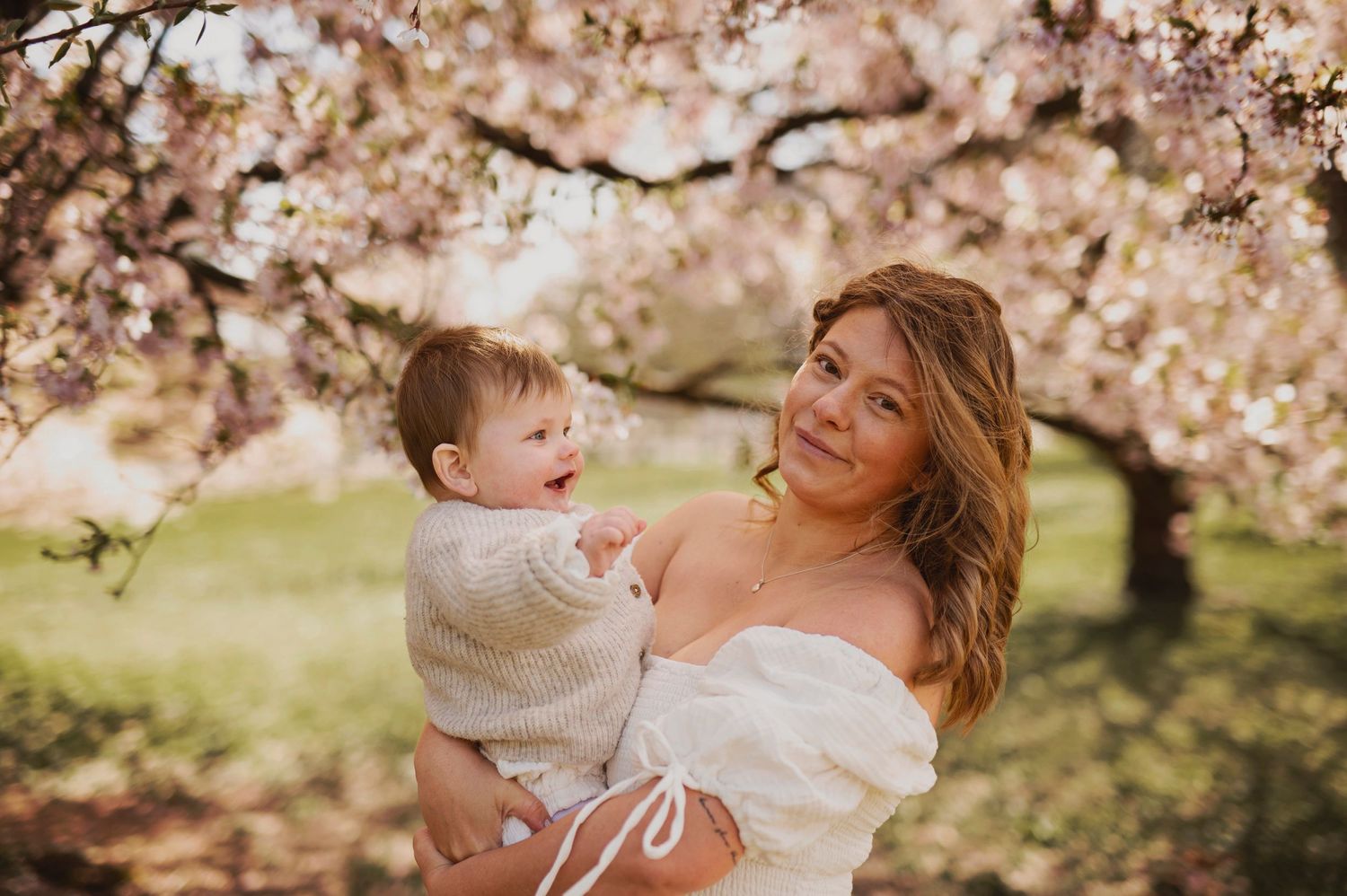 Mother and child share joyful moment under blooming cherry blossoms in spring garden setting.