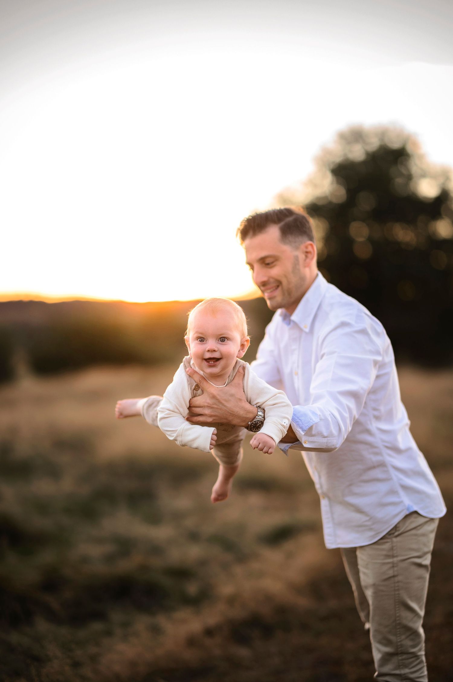 A joyful moment captured at sunset as a baby is lifted playfully in the air.