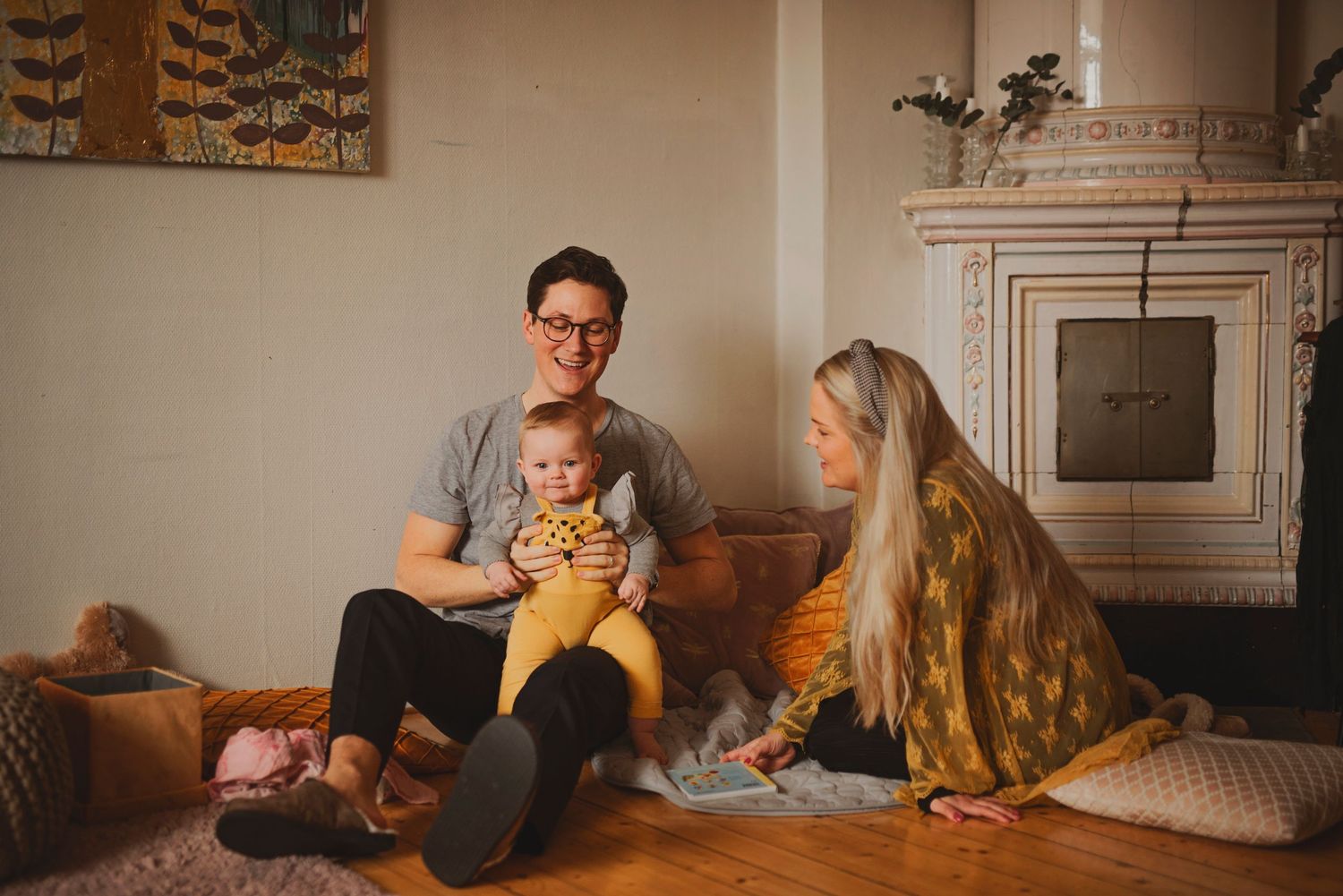 Happy young family with baby sitting together in cozy living room by fireplace.