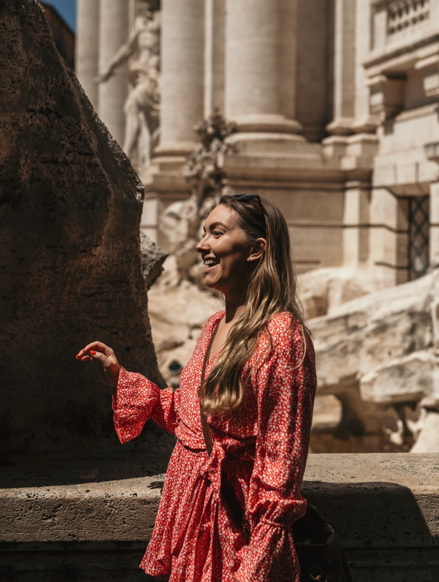 Woman in red floral dress smiling at Trevi Fountain Rome Italy.