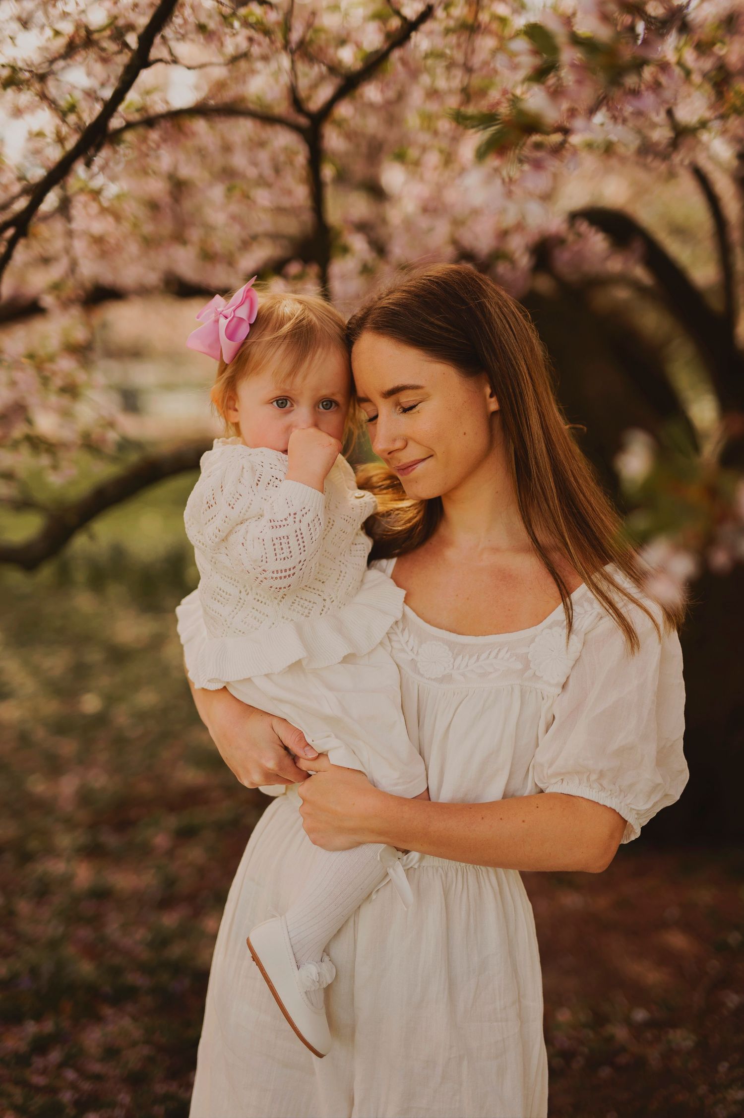 Sweet spring portrait under cherry blossoms with matching white dresses.
