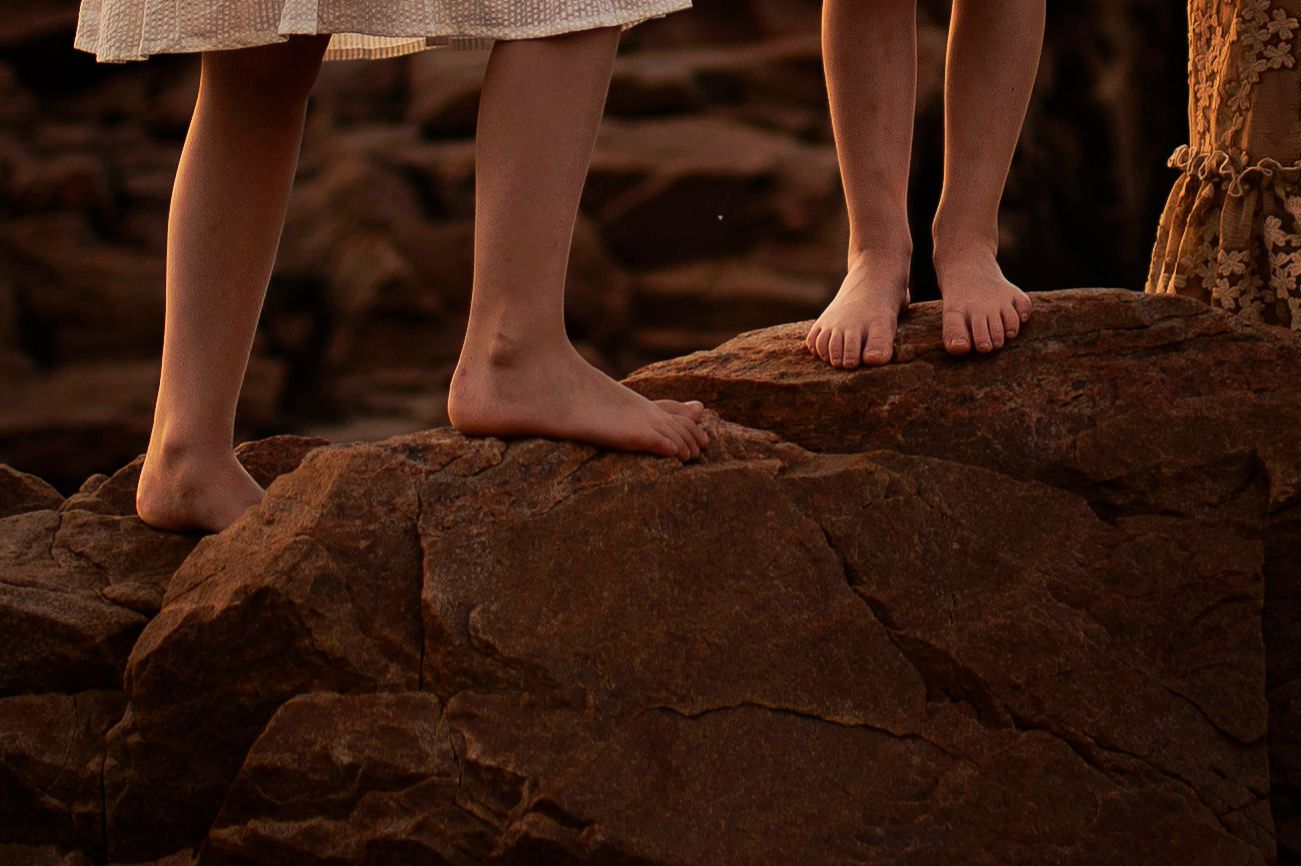 Bare feet standing on rugged coastal rocks in warm lighting.
