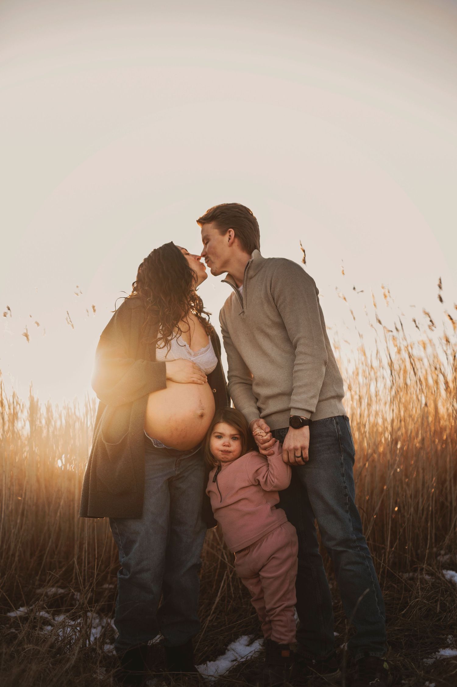 Family maternity moment captured at sunset among winter reeds and grass.